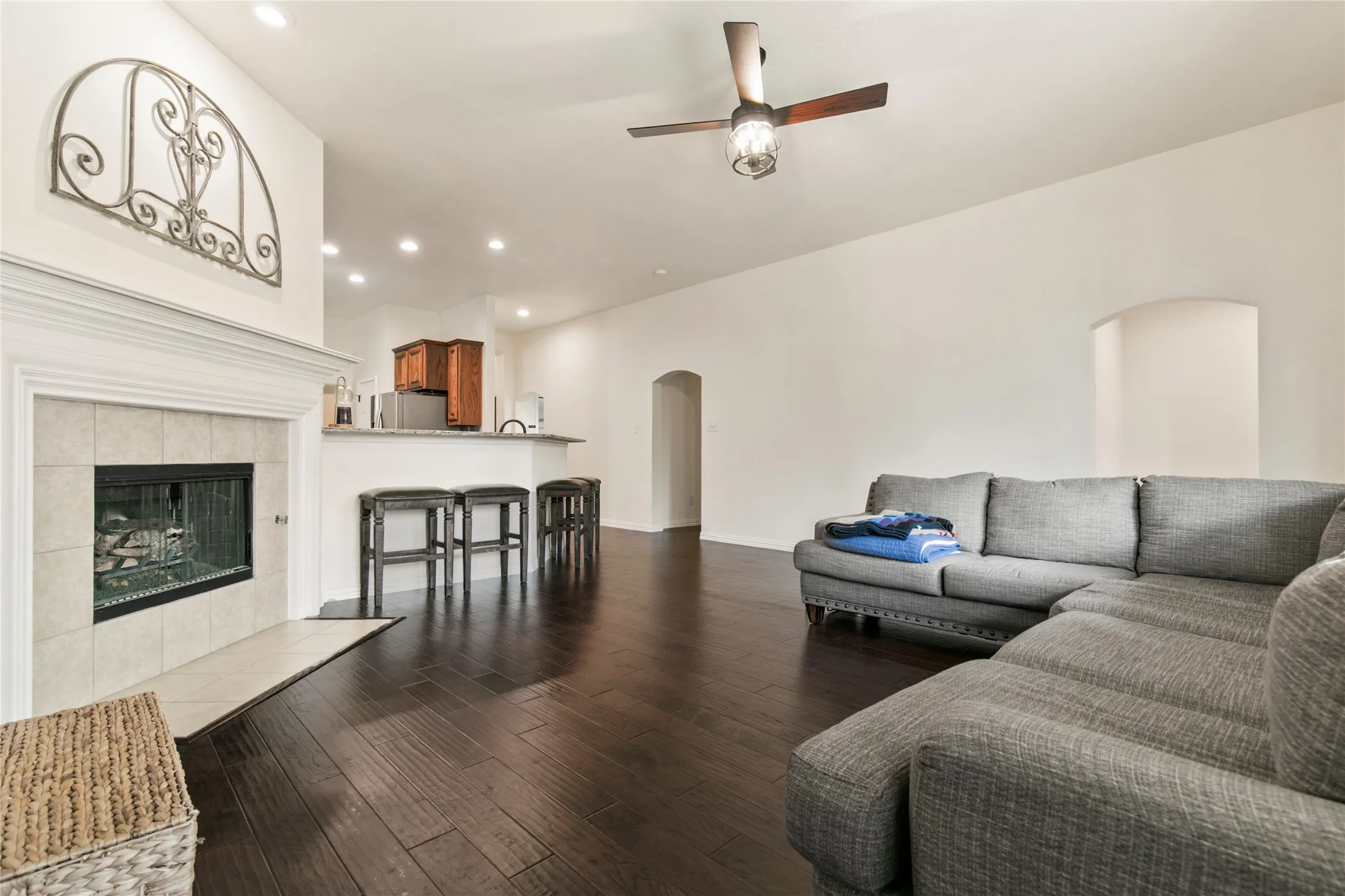 Living area featuring dark wood-finish flooring, a tile-surround fireplace with a white mantel, and a breakfast bar with a light-toned countertop