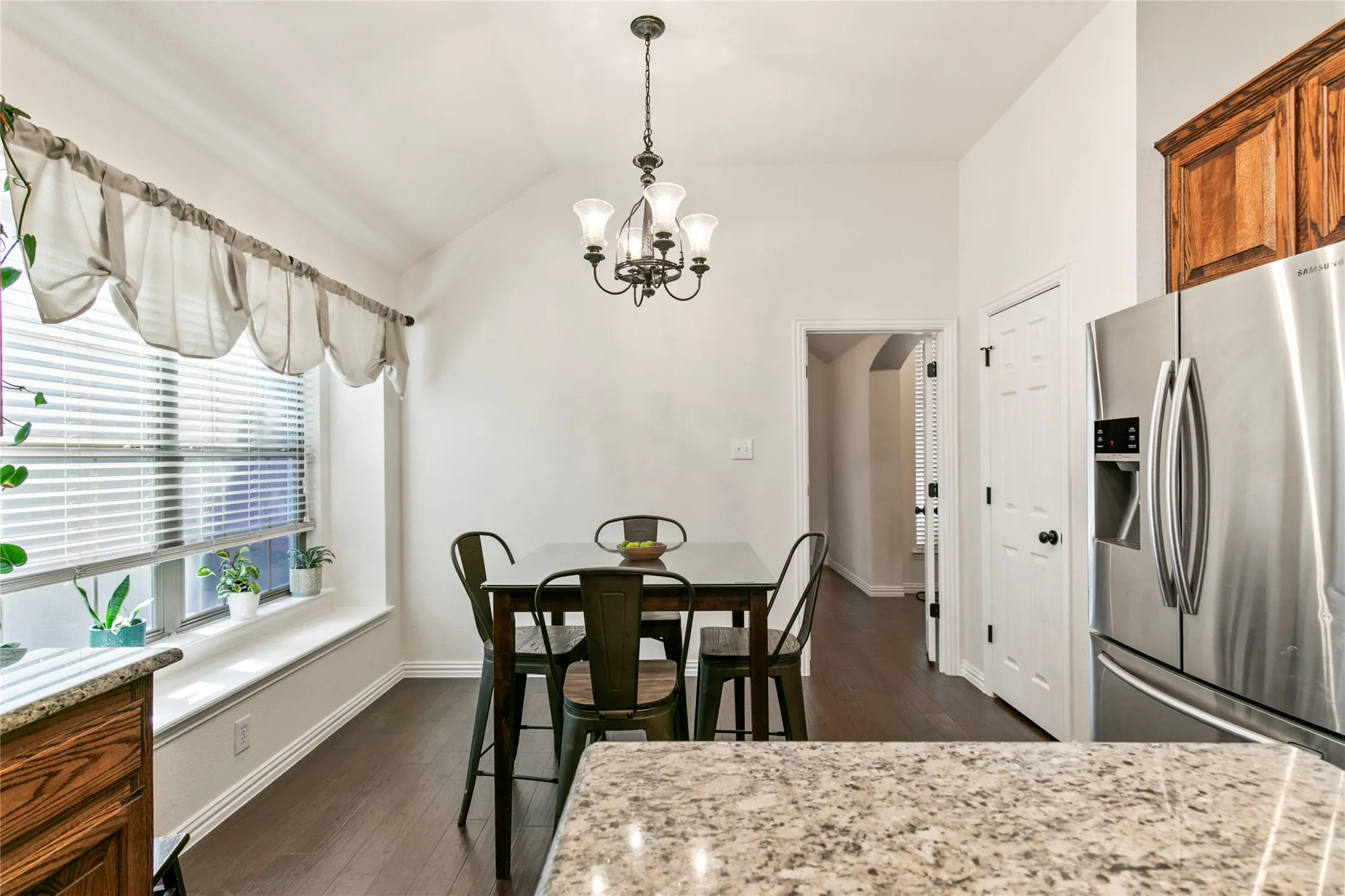 Dining area featuring wood-finish flooring, a white trim window with blinds and a deep sill, a five-light chandelier, and vaulted ceilings
