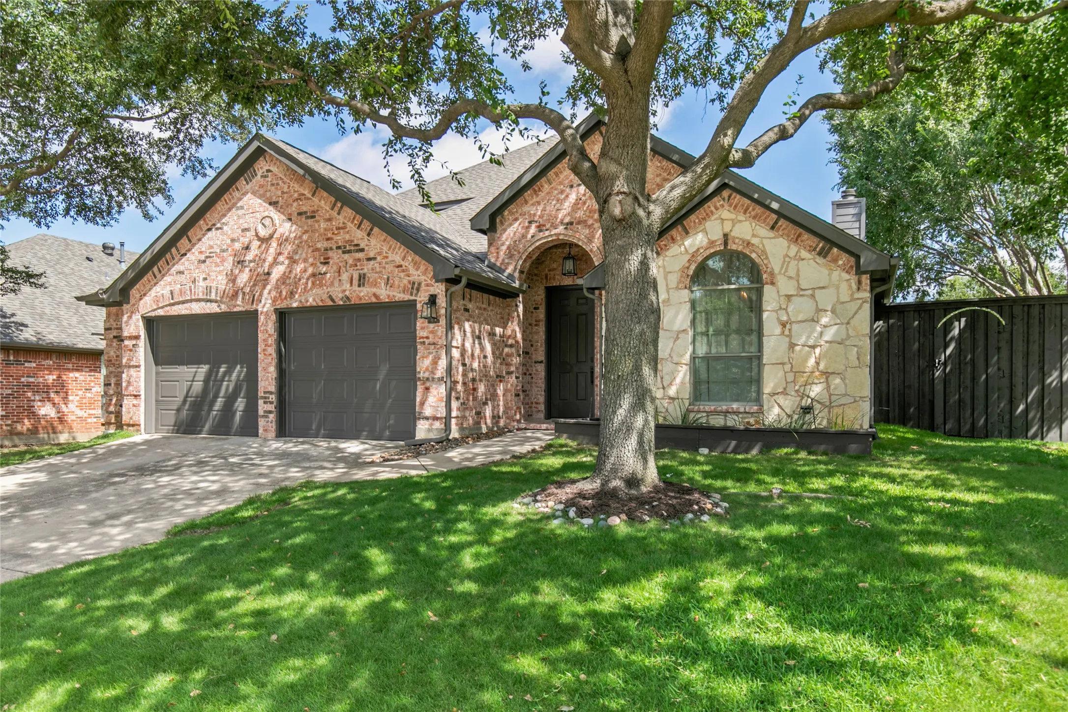 Brick and stone facade residence featuring a two-car garage, arched entryways, and a mature shade tree