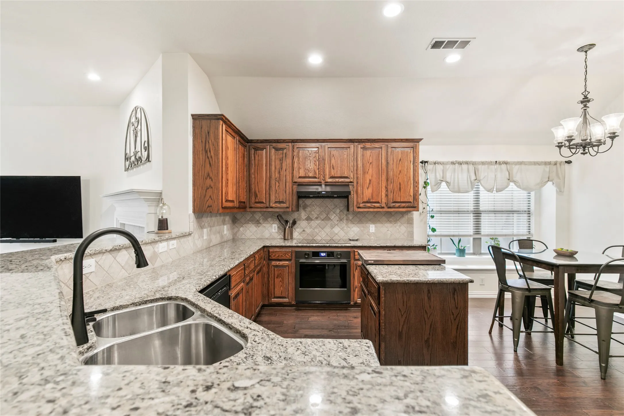 Kitchen featuring granite countertops, wood-finish cabinetry, an integrated oven, and a tiled backsplash