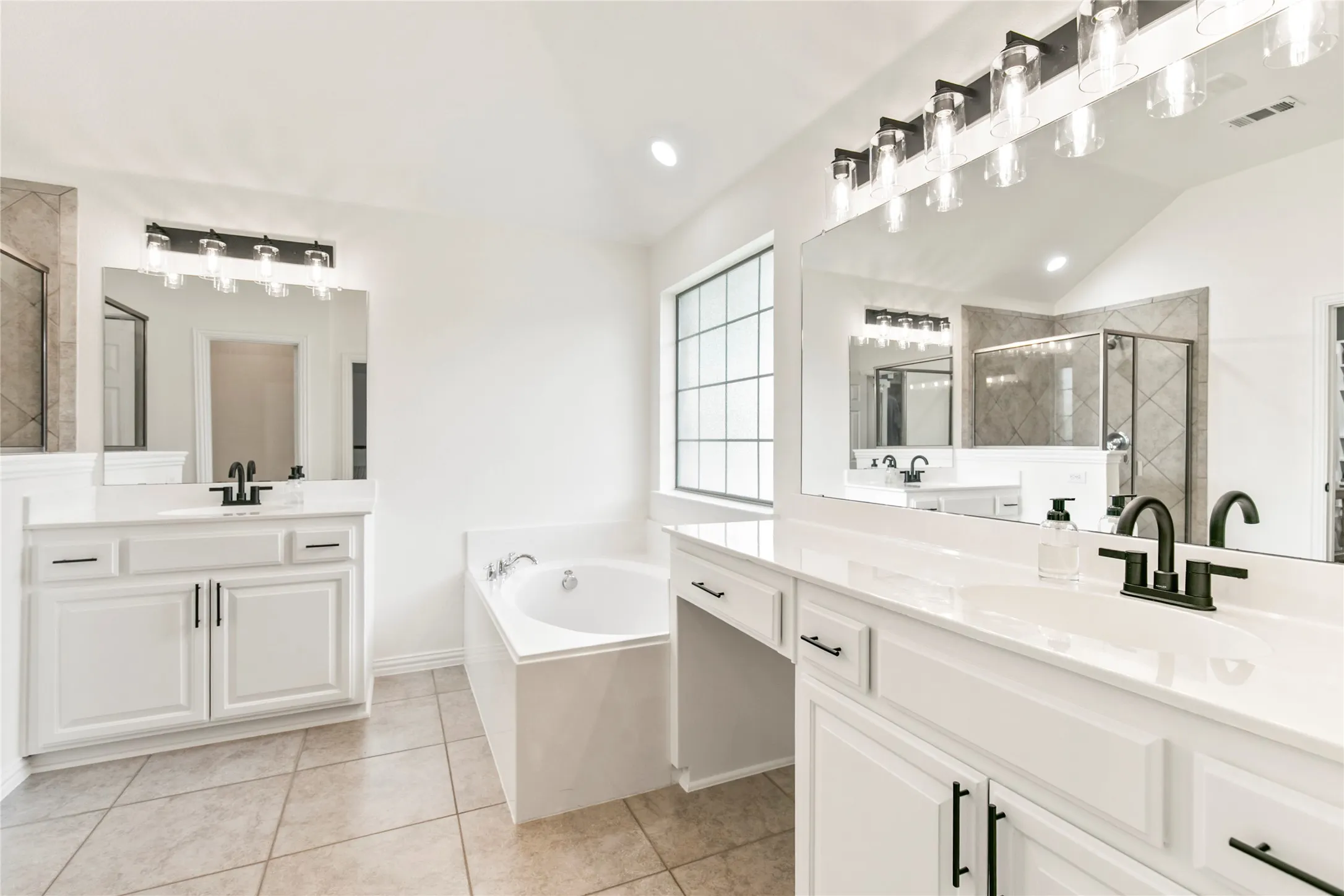 Bathroom featuring dual vanities with white cabinetry, light-toned countertops, and matte black fixtures