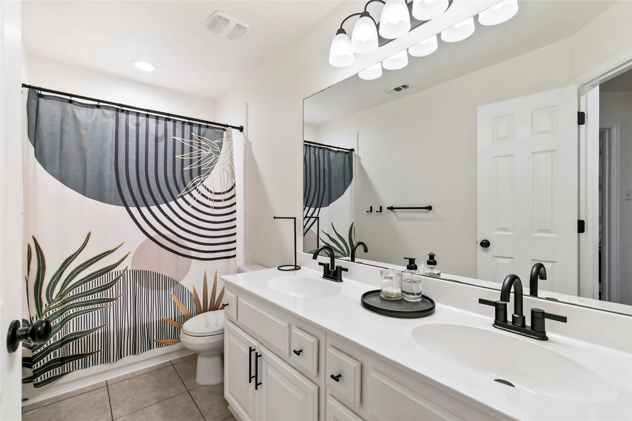 Dual vanity featuring white cabinetry, integrated sinks, black hardware, and an expansive mirror