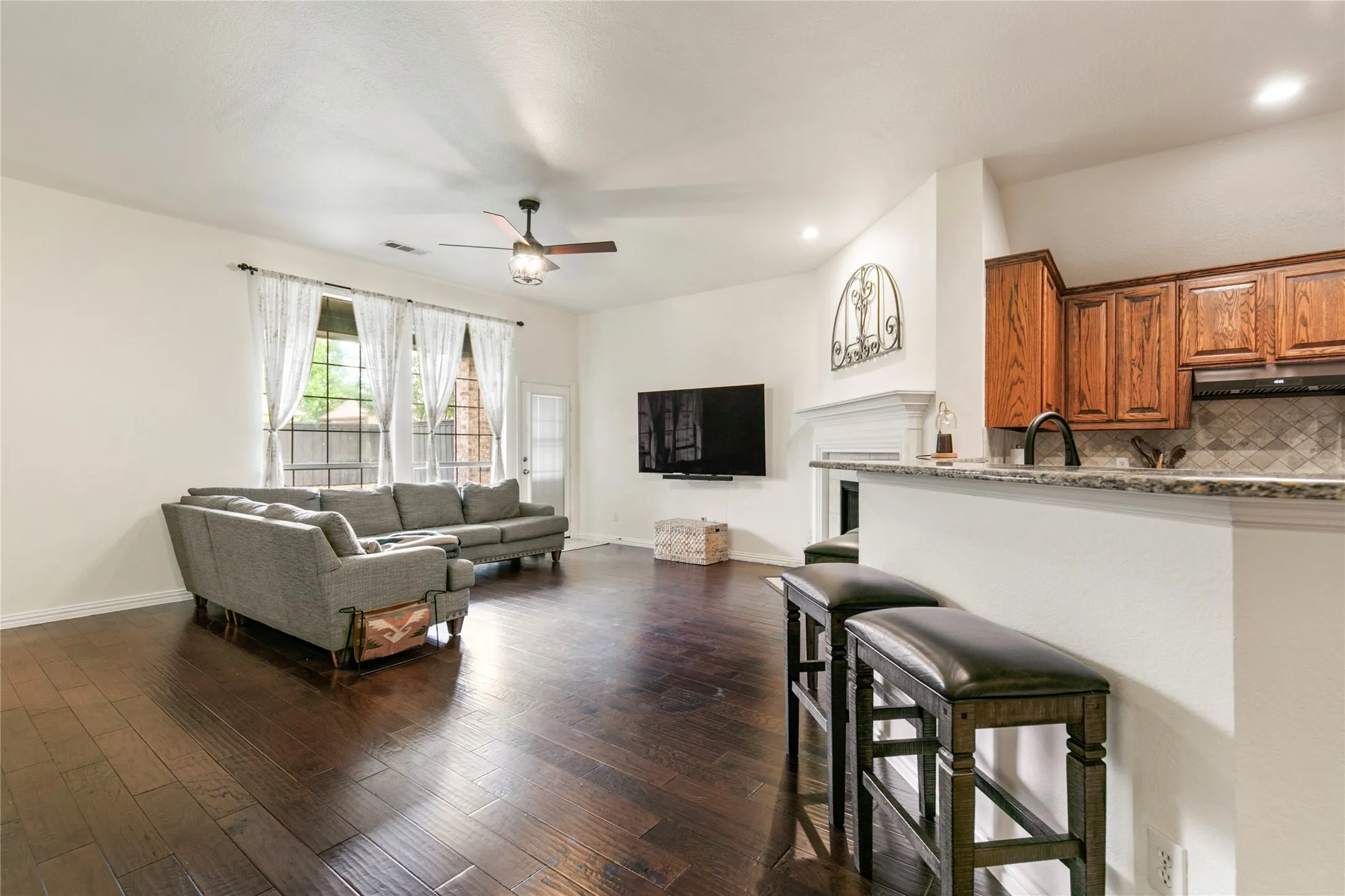 Open-concept living area featuring wood-finish flooring, a ceiling fan with integrated lighting, a white painted fireplace mantel, and recessed lighting