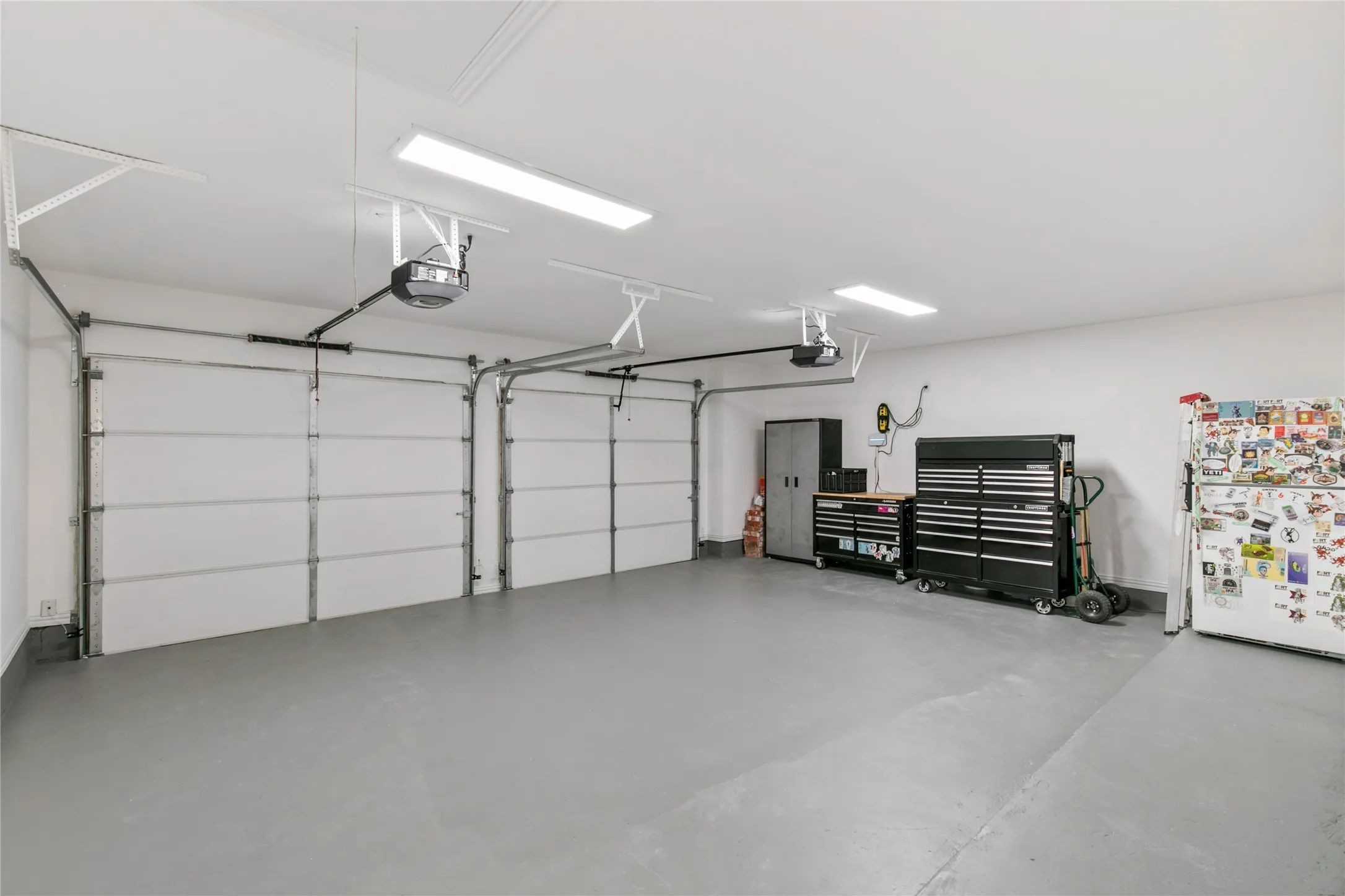 Two-car garage featuring a painted concrete floor, two individual garage doors with openers, and overhead strip lighting
