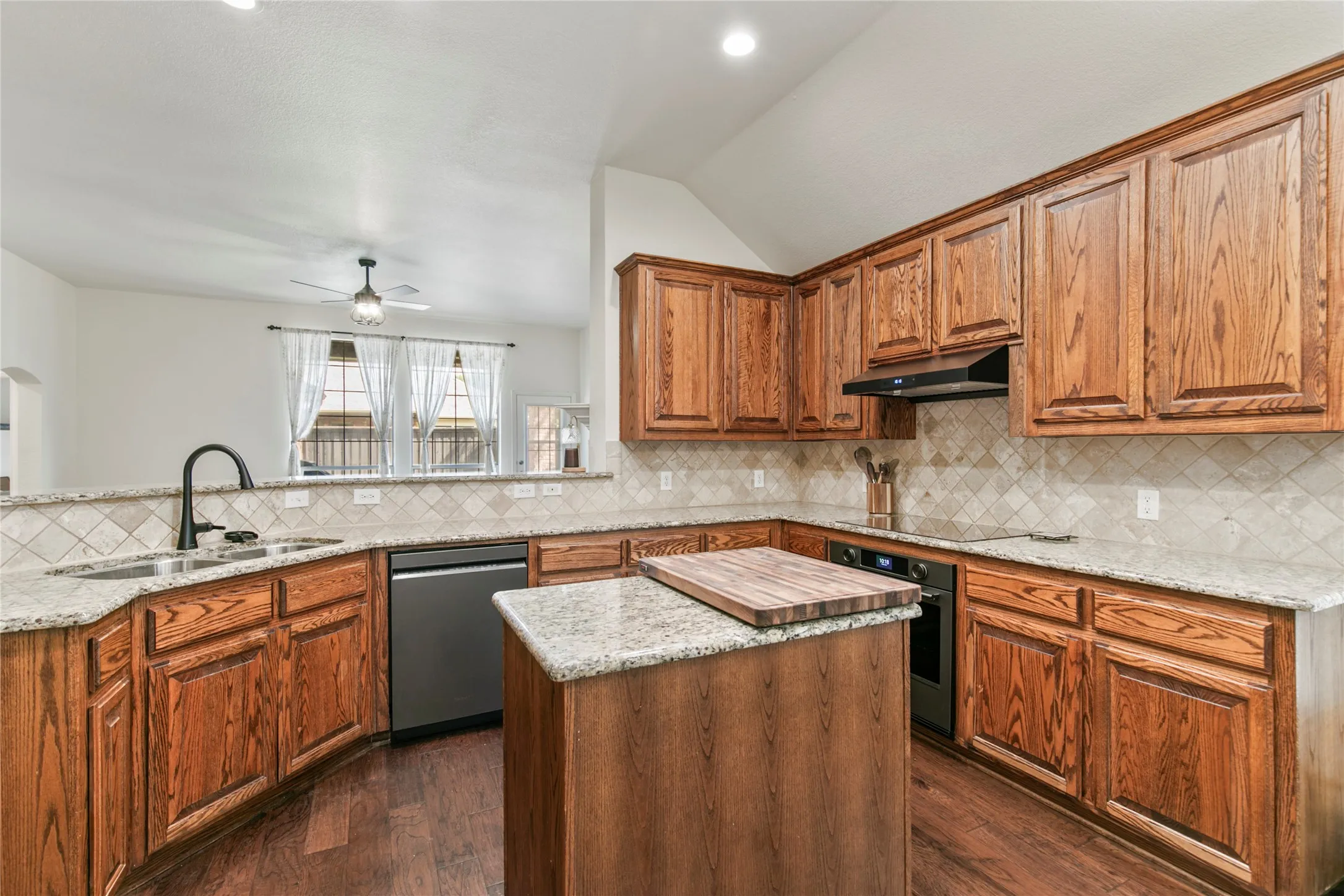 Kitchen featuring wood cabinetry, granite countertops, tile backsplash, built-in stainless steel appliances, and a central island