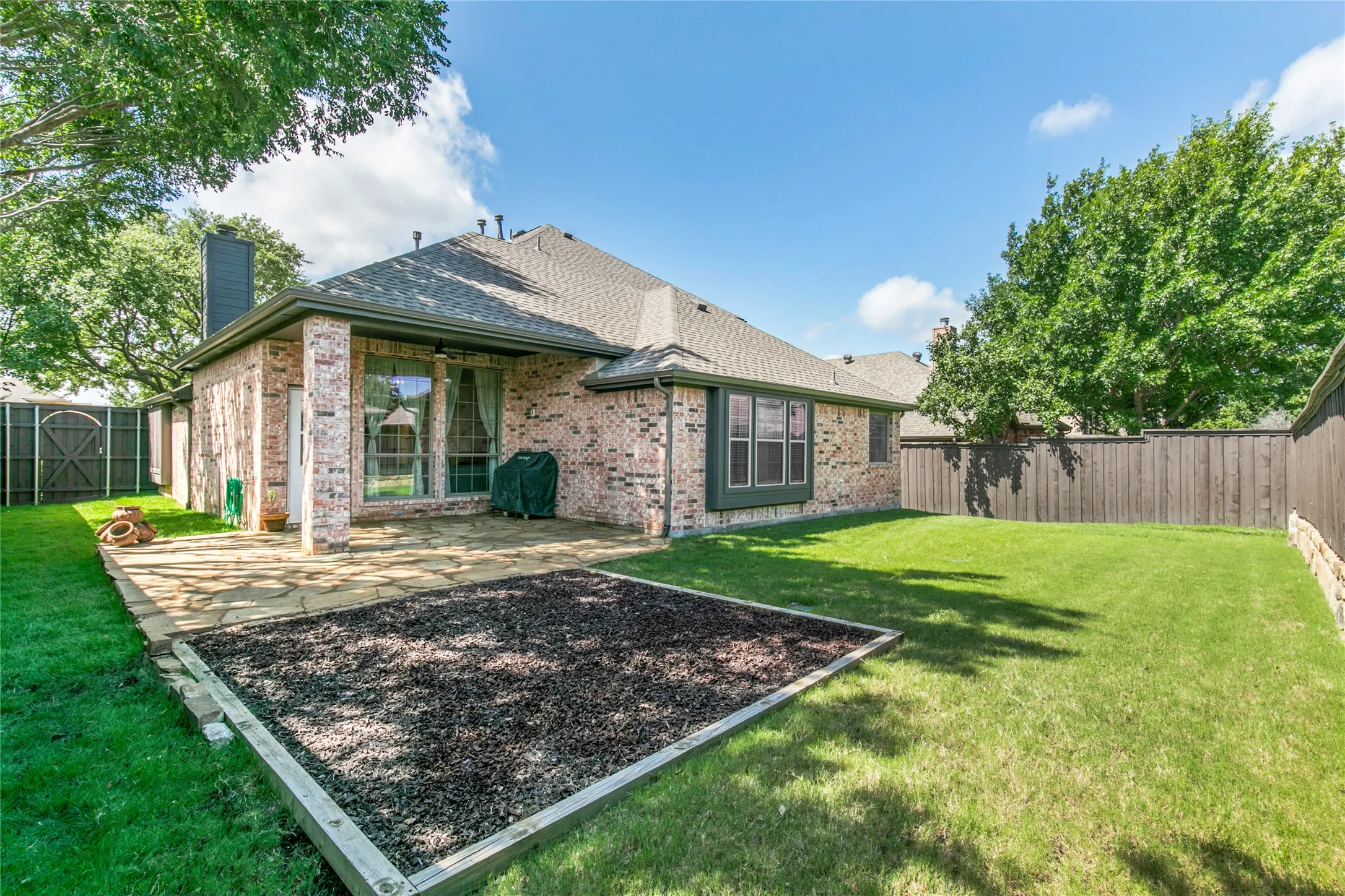 Expansive backyard featuring a stone patio, a raised garden bed, a privacy fence, and mature trees