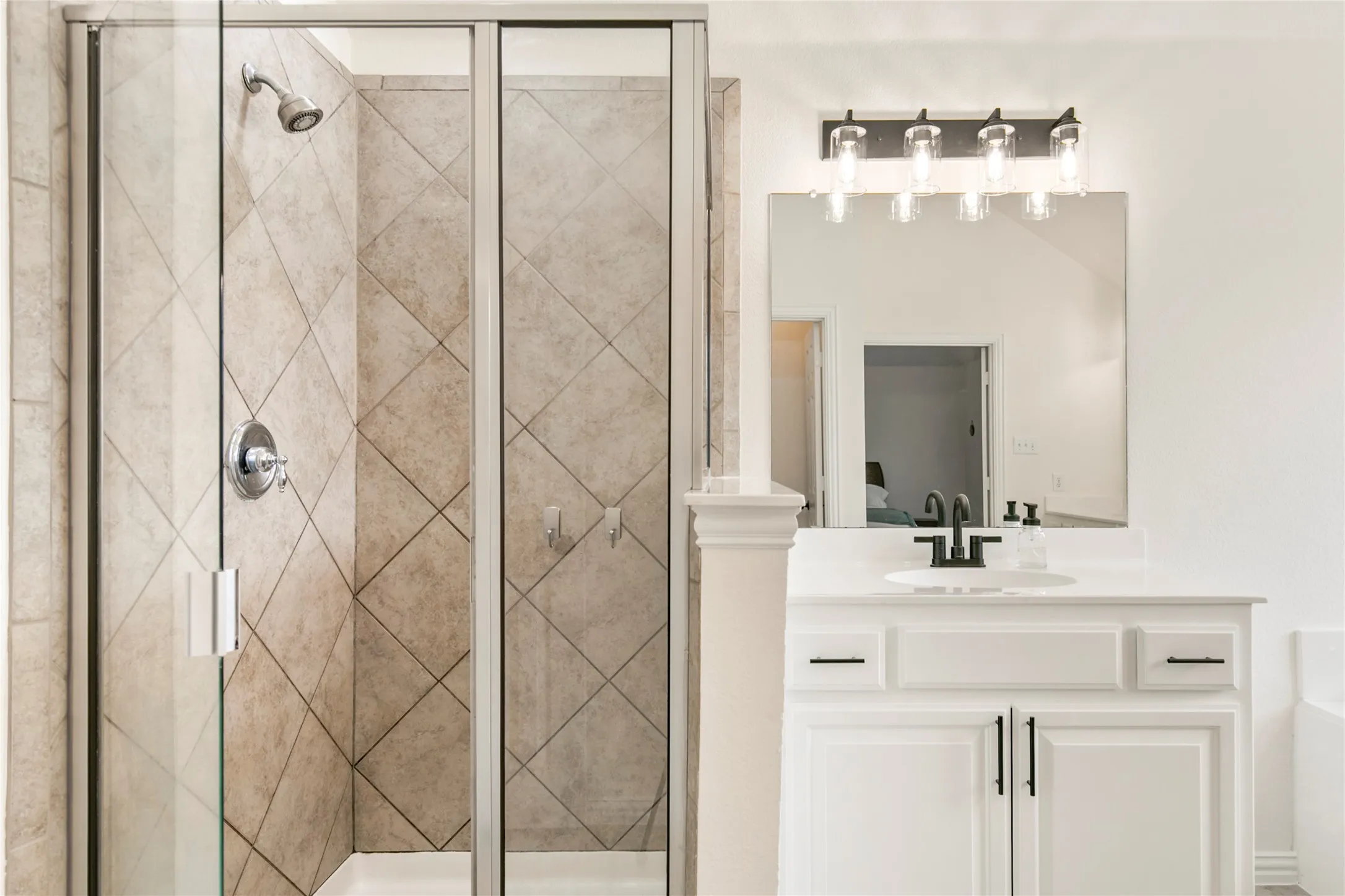 Glass-enclosed shower with tiled walls, chrome fixtures, and a dedicated vanity featuring a single sink, light-colored countertop, white cabinetry, and matte black hardware
