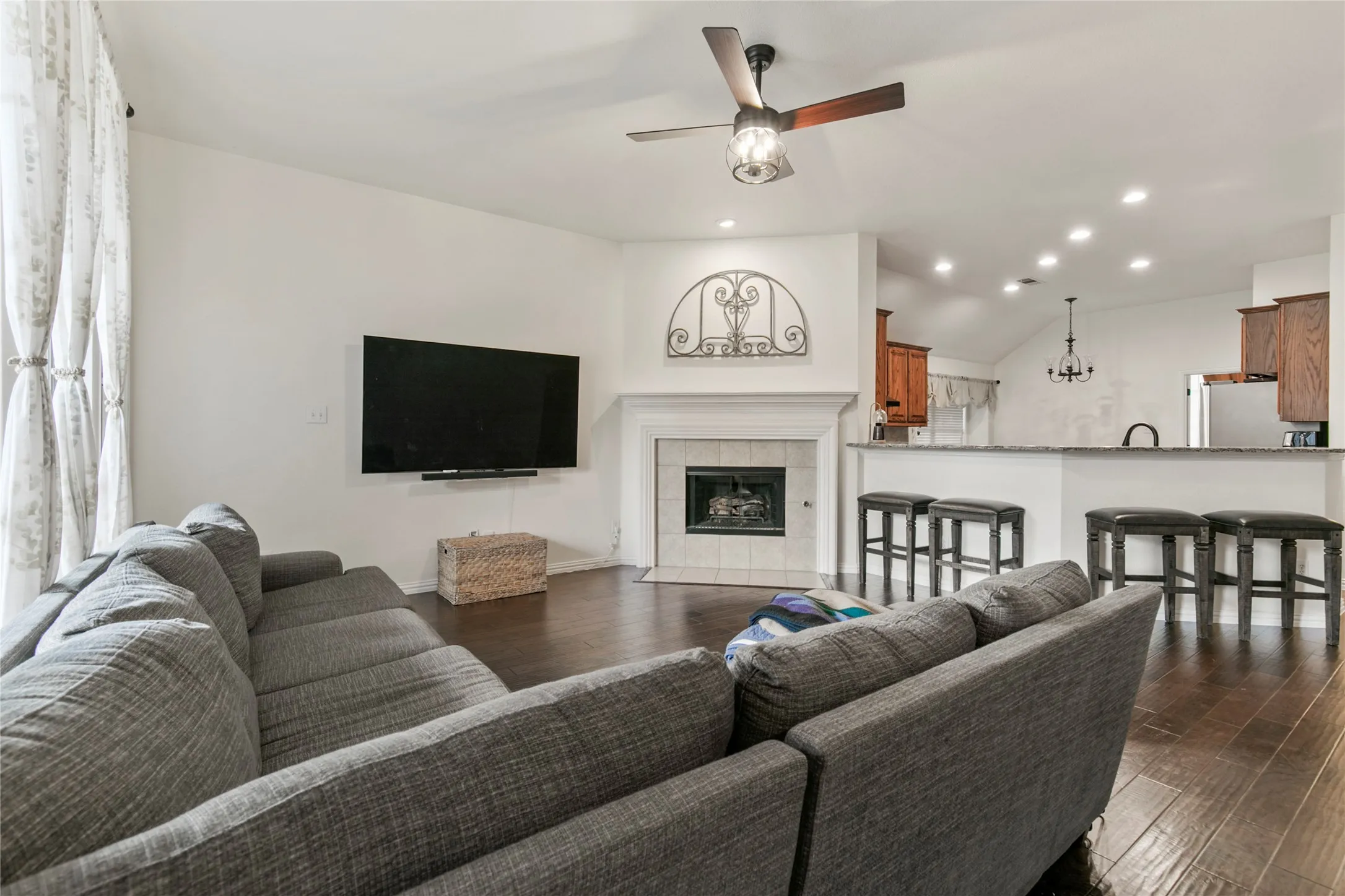 Living area featuring wood-finish flooring, a white-mantled fireplace, and a ceiling fan