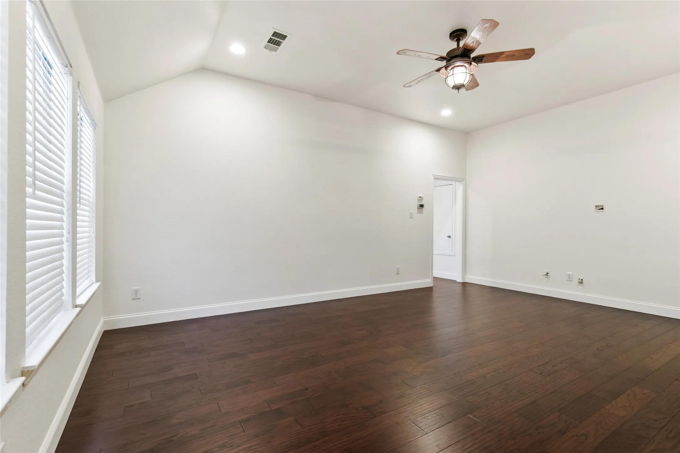 Spacious room featuring vaulted ceilings, dark wood-finish flooring, recessed lighting, and a ceiling fan with integrated light
