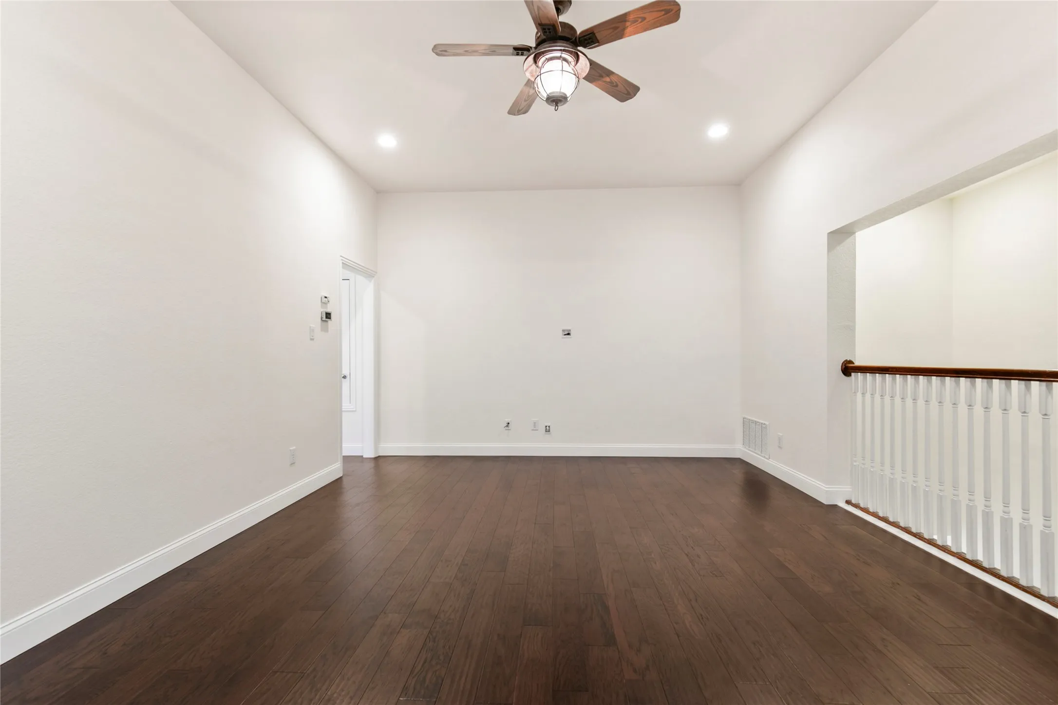 Spacious room featuring high ceilings, recessed lighting, wood-finish flooring, a ceiling fan, and a built-in railing system