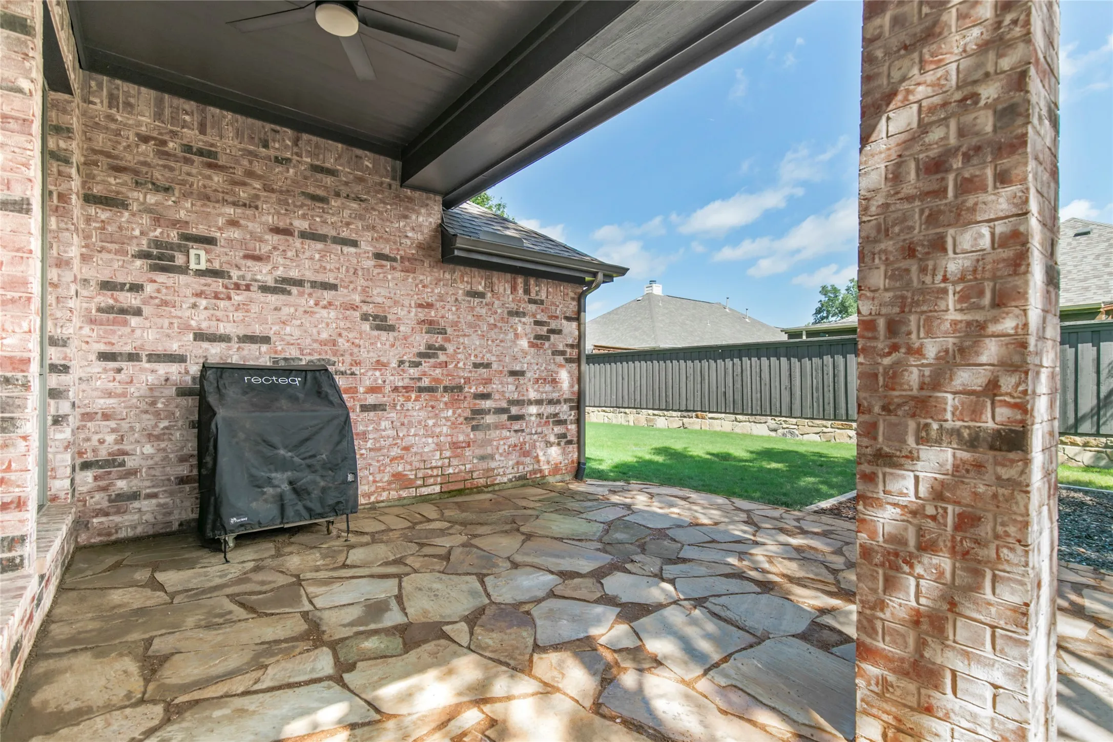 Covered patio featuring a ceiling fan, flagstone flooring, and a brick exterior