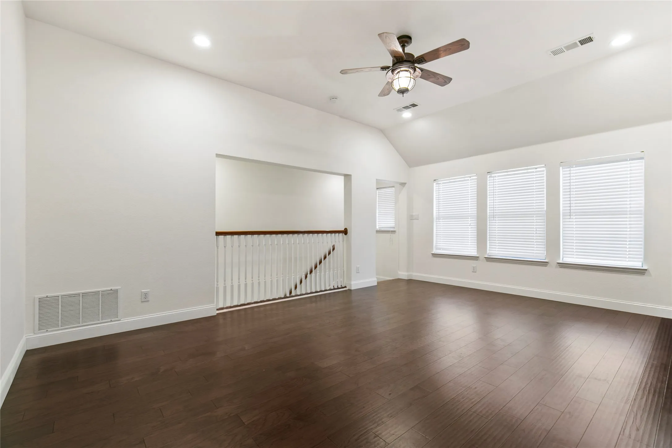 Spacious room featuring vaulted ceilings, wood-finish flooring, recessed lighting, a ceiling fan with light fixture, and three windows with horizontal blinds