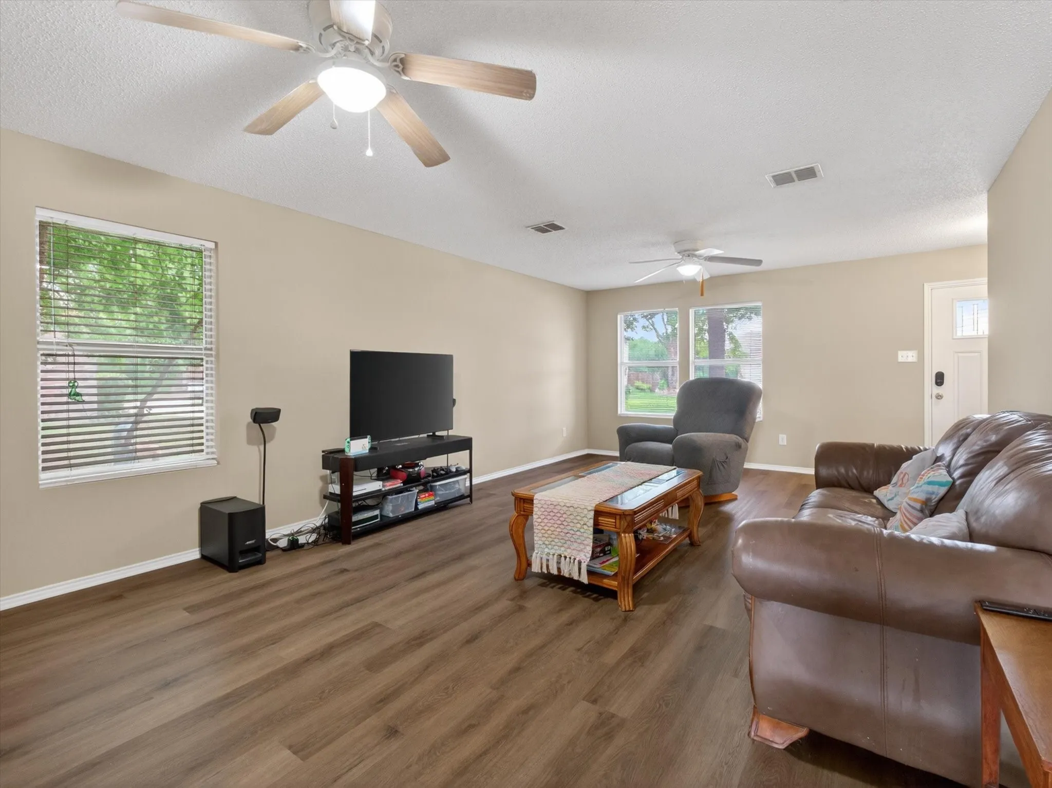 Spacious living area featuring wood-finish flooring, neutral wall tones, and multiple windows
