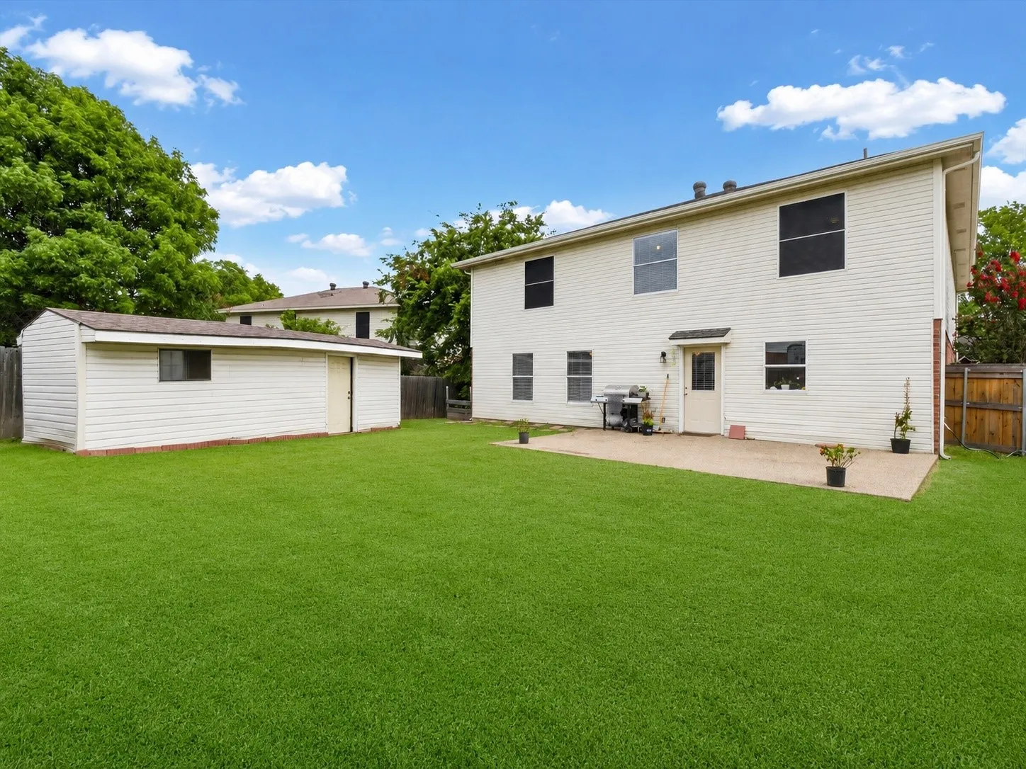 Expansive green lawn with a white vinyl-sided storage shed and a concrete patio at the rear of the residence