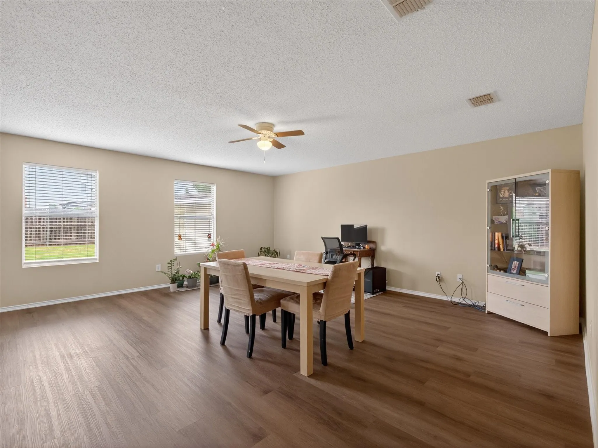Spacious living area featuring wood-finish flooring, neutral wall tones, and multiple windows with blinds