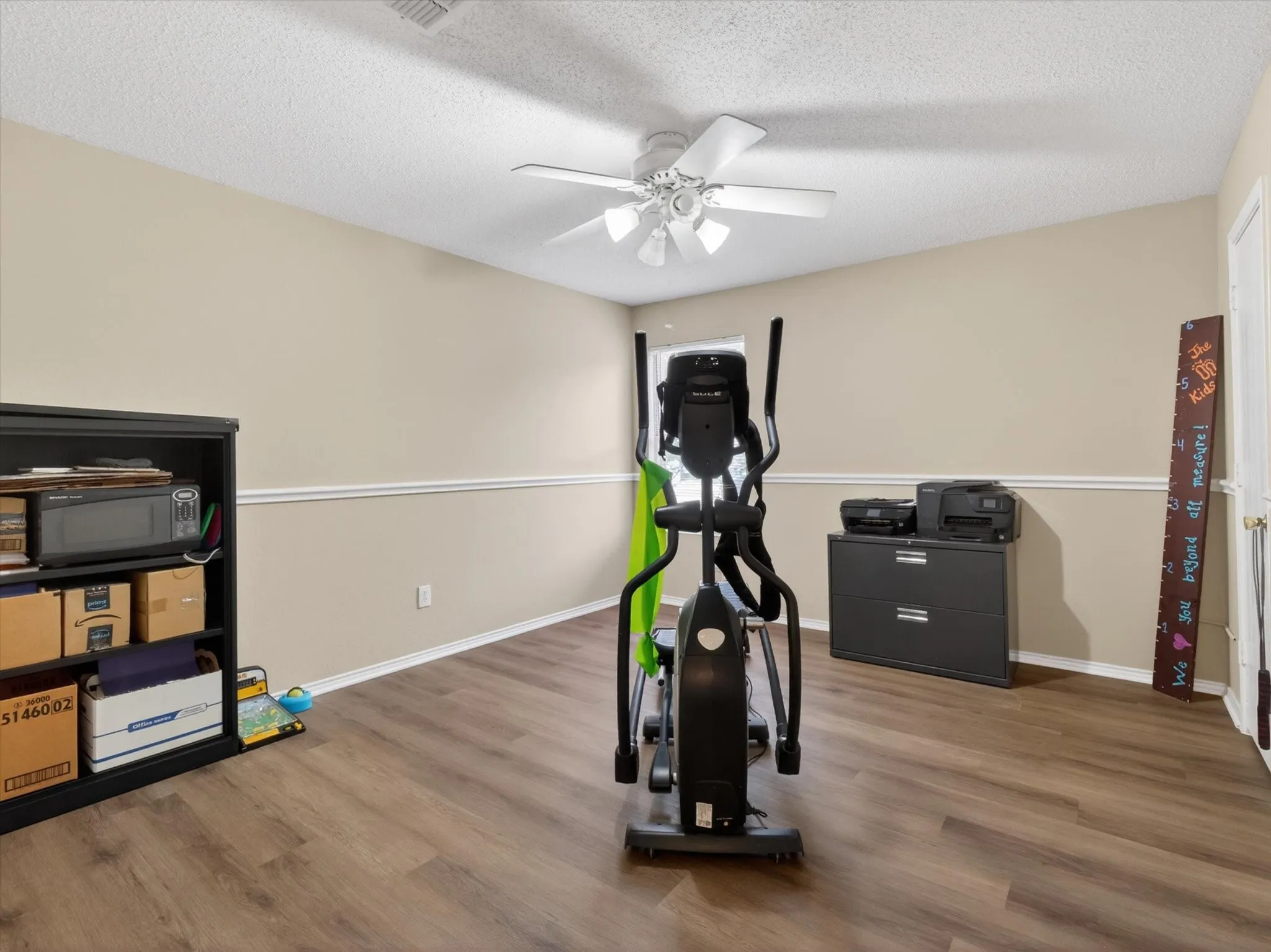 Spacious room featuring wood-finish flooring, neutral wall tones, a ceiling fan with integrated lighting, and white baseboards with chair rail molding