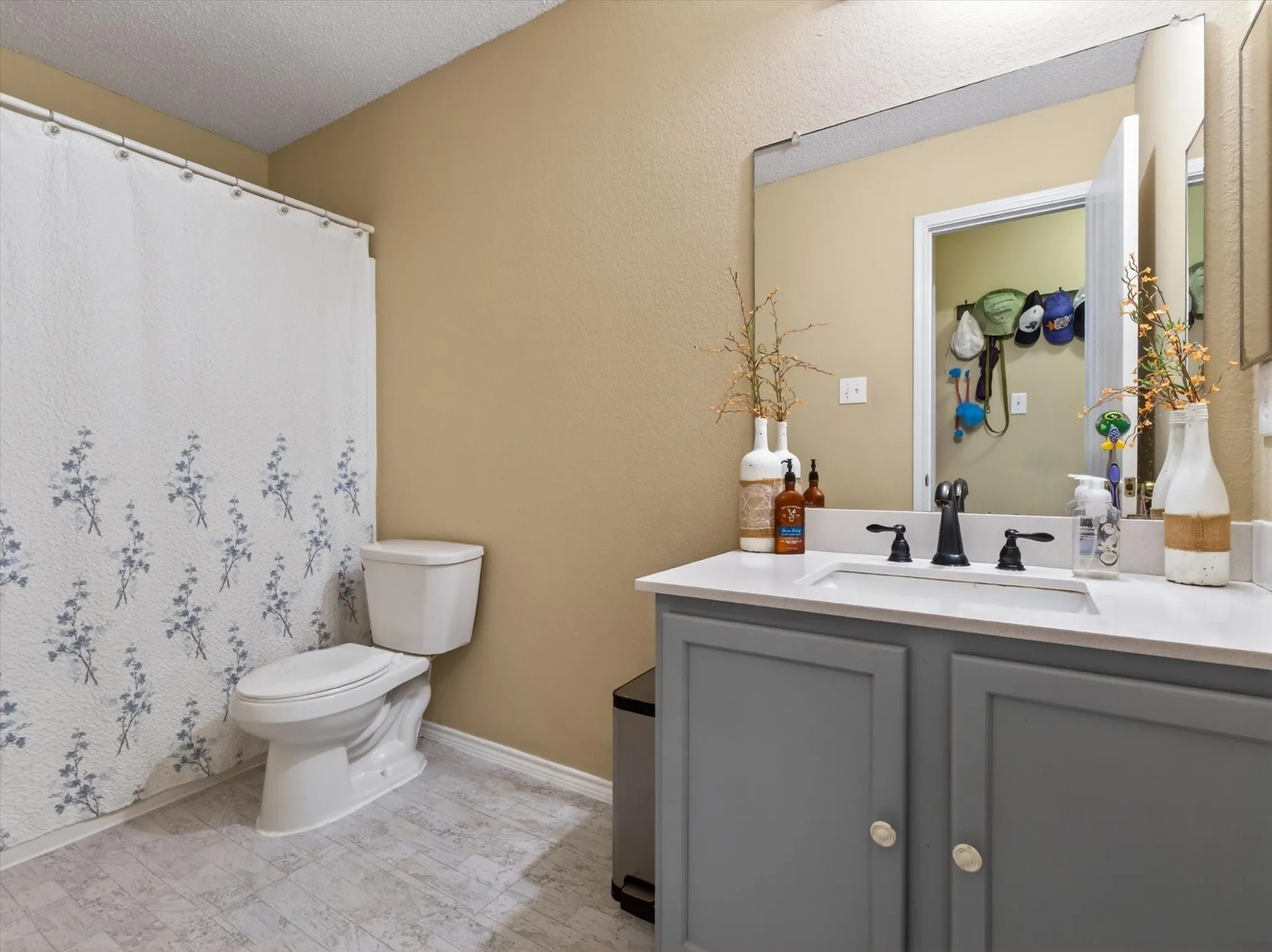 Bathroom featuring a vanity with a white countertop and gray cabinetry, a rectangular undermount sink with a black faucet, a large wall-mounted mirror, and light-toned flooring