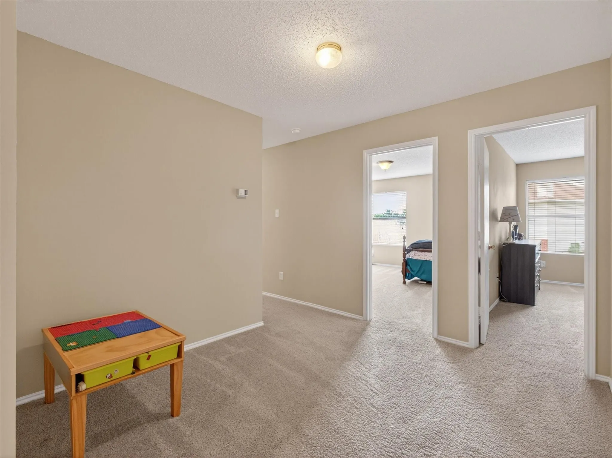 Carpeted hallway with neutral wall paint and white trim, featuring two open doorways revealing additional rooms