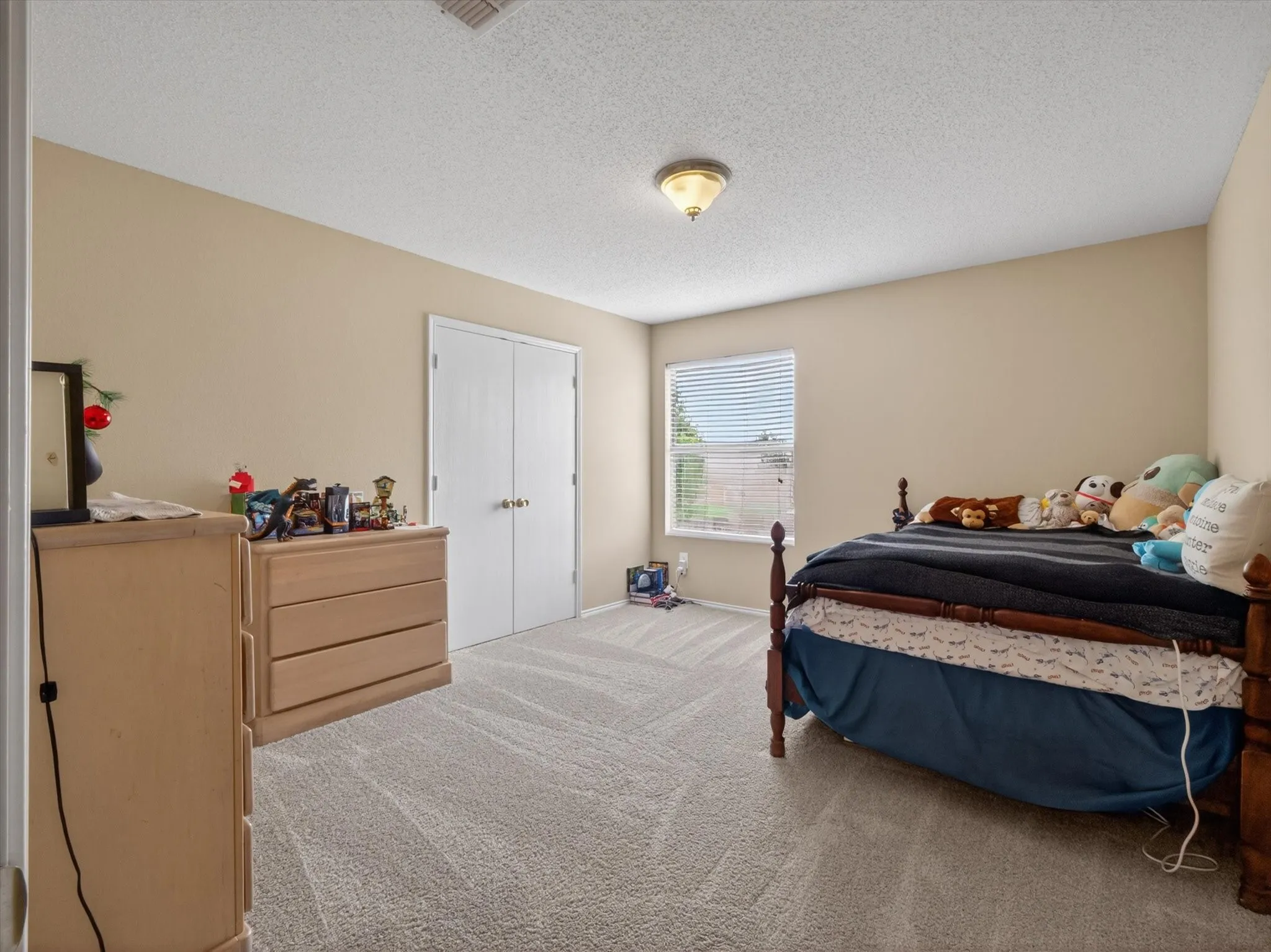 Carpeted room featuring a double-door closet, a single window with horizontal blinds, and a ceiling-mounted light fixture