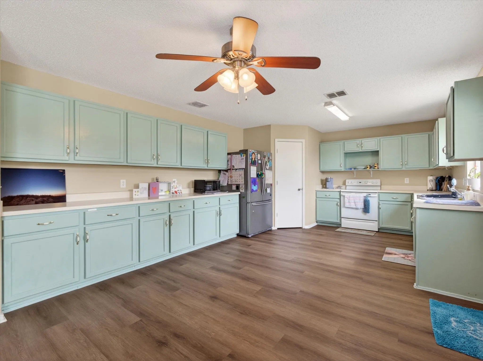 Kitchen featuring extensive light blue cabinetry with brushed nickel hardware, light countertops, wood-finish flooring, and a ceiling fan with integrated lighting