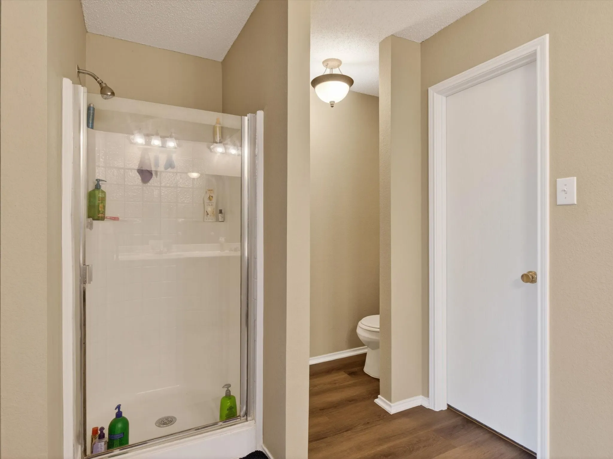 Glass-enclosed shower stall with a textured tile surround and chrome fixtures