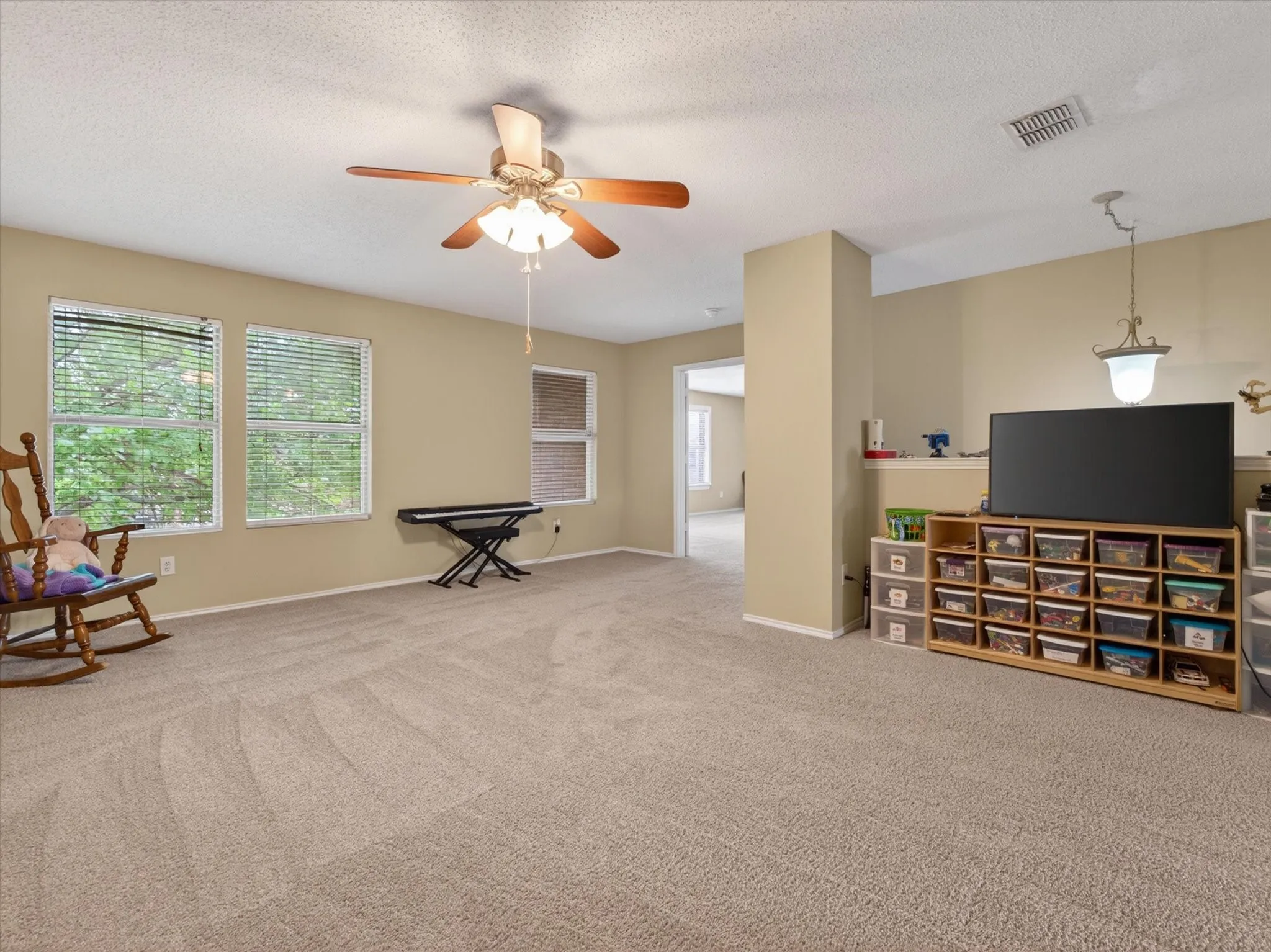 Spacious room featuring neutral carpeting, multiple windows with blinds, a ceiling fan with integrated lighting, and recessed lighting