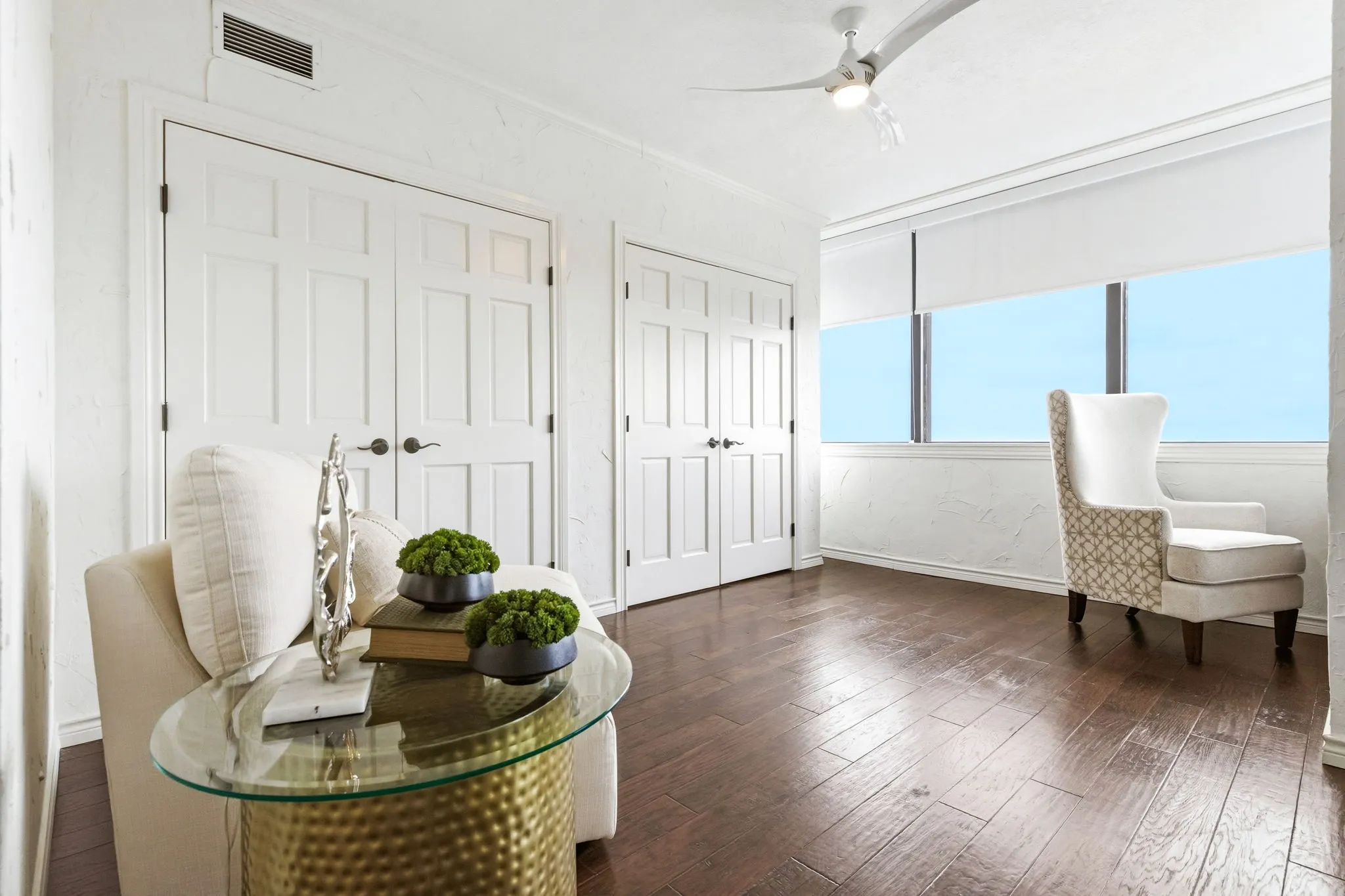 Spacious room featuring wood-finish flooring, multiple paneled doors, and a ceiling fan with integrated lighting