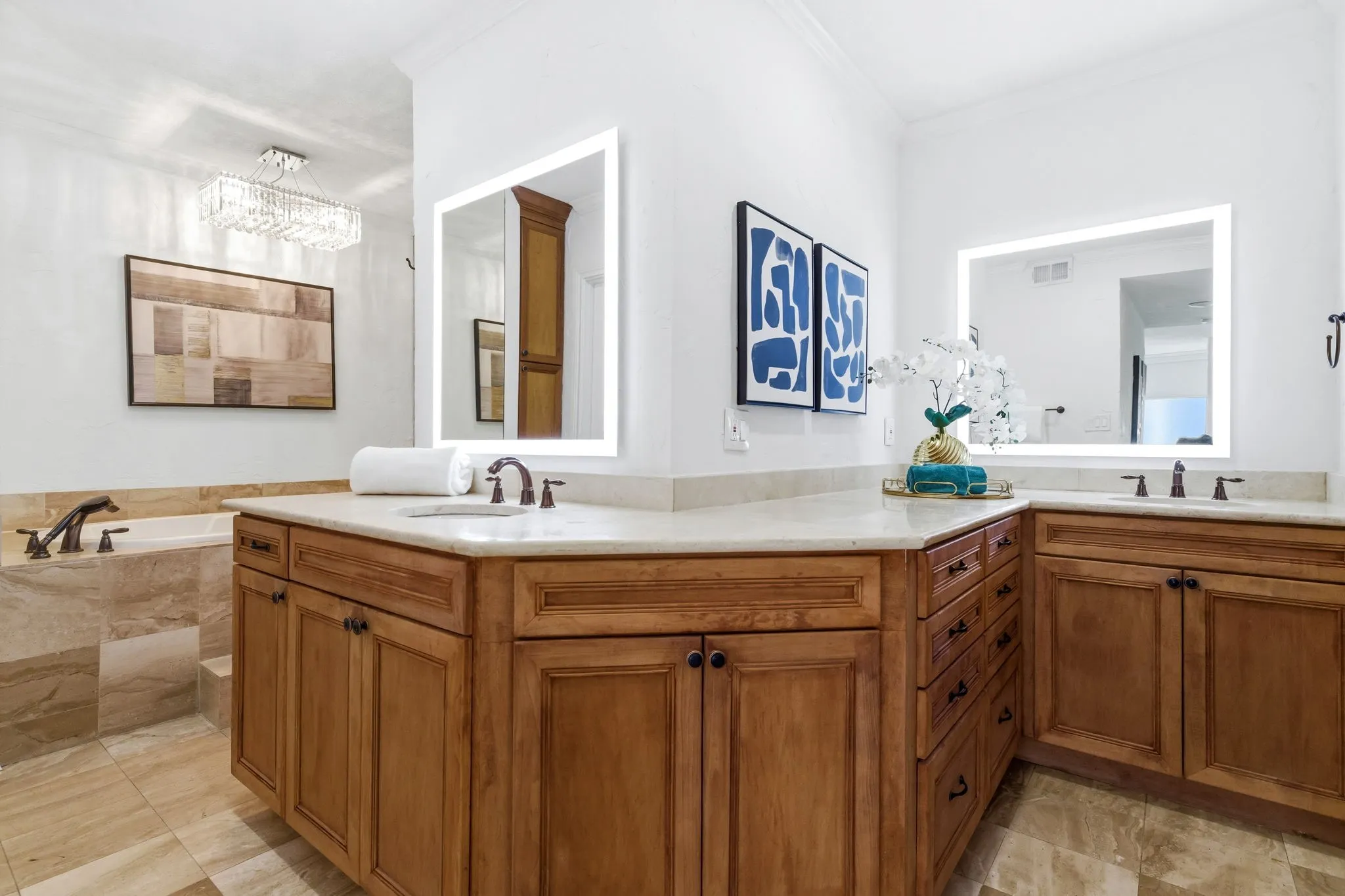 Spacious bathroom featuring twin wood-finish vanities with light-toned countertops, integrated sinks, and illuminated mirrors