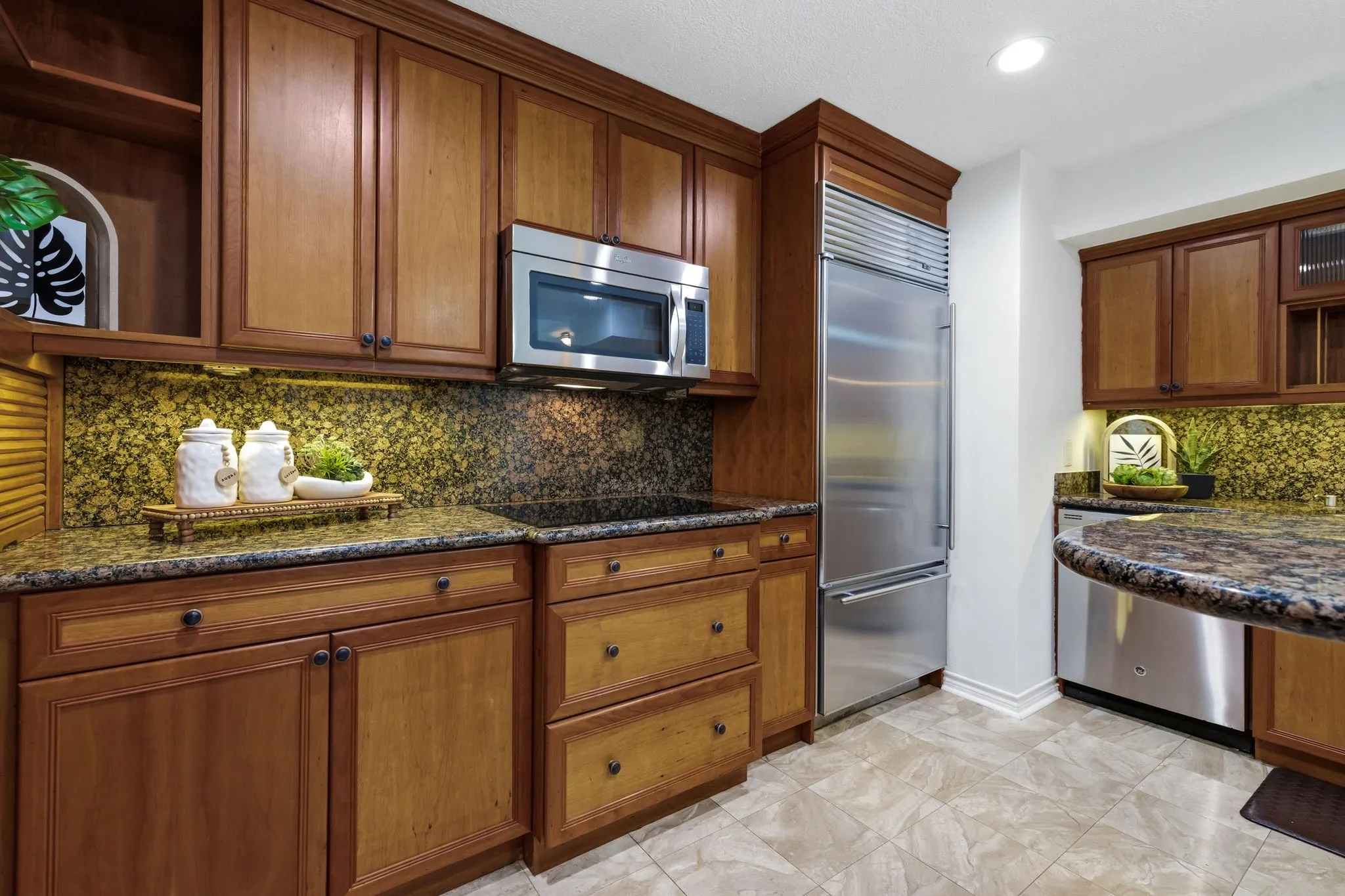 Kitchen featuring wood cabinetry, stainless steel appliances, speckled stone countertops, and a matching backsplash