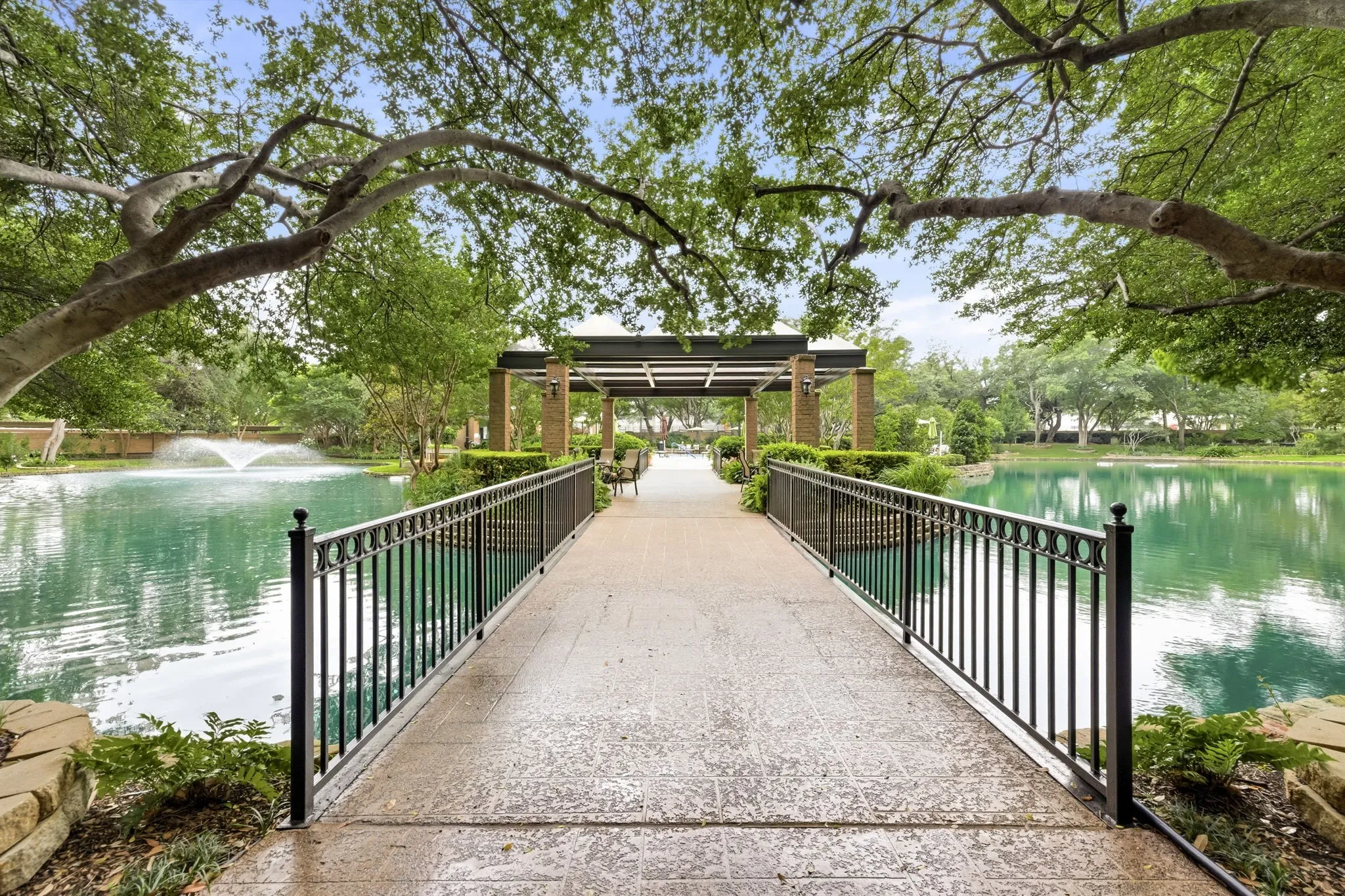 Concrete pathway bridging a tranquil pond with a decorative fountain