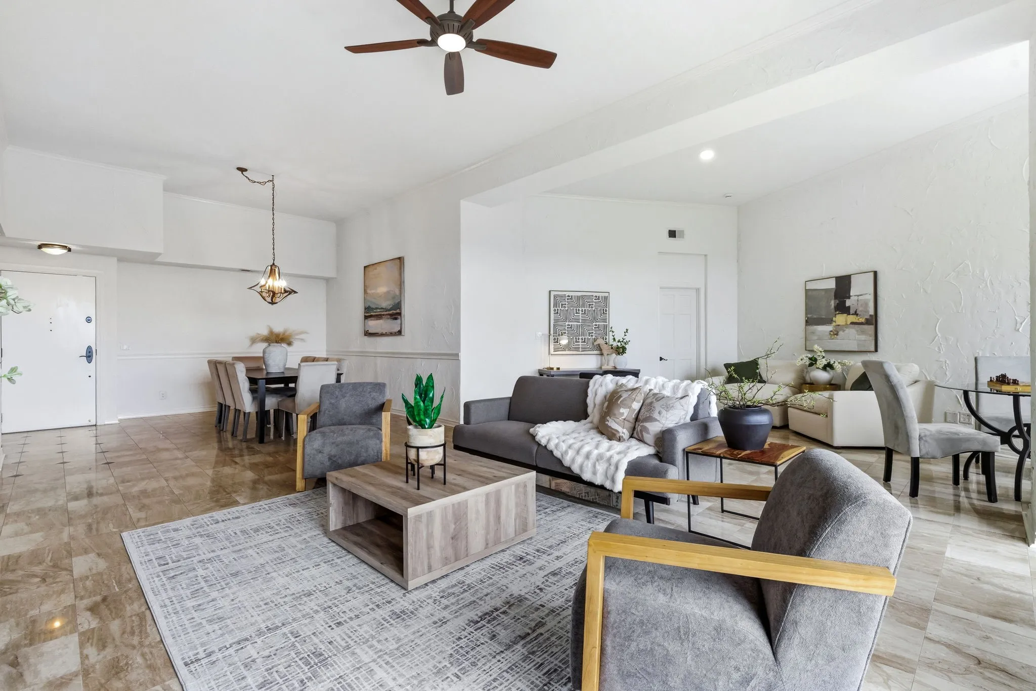 Open-concept living space featuring wood-finish flooring, a dining area with a chandelier, a ceiling fan, and white walls