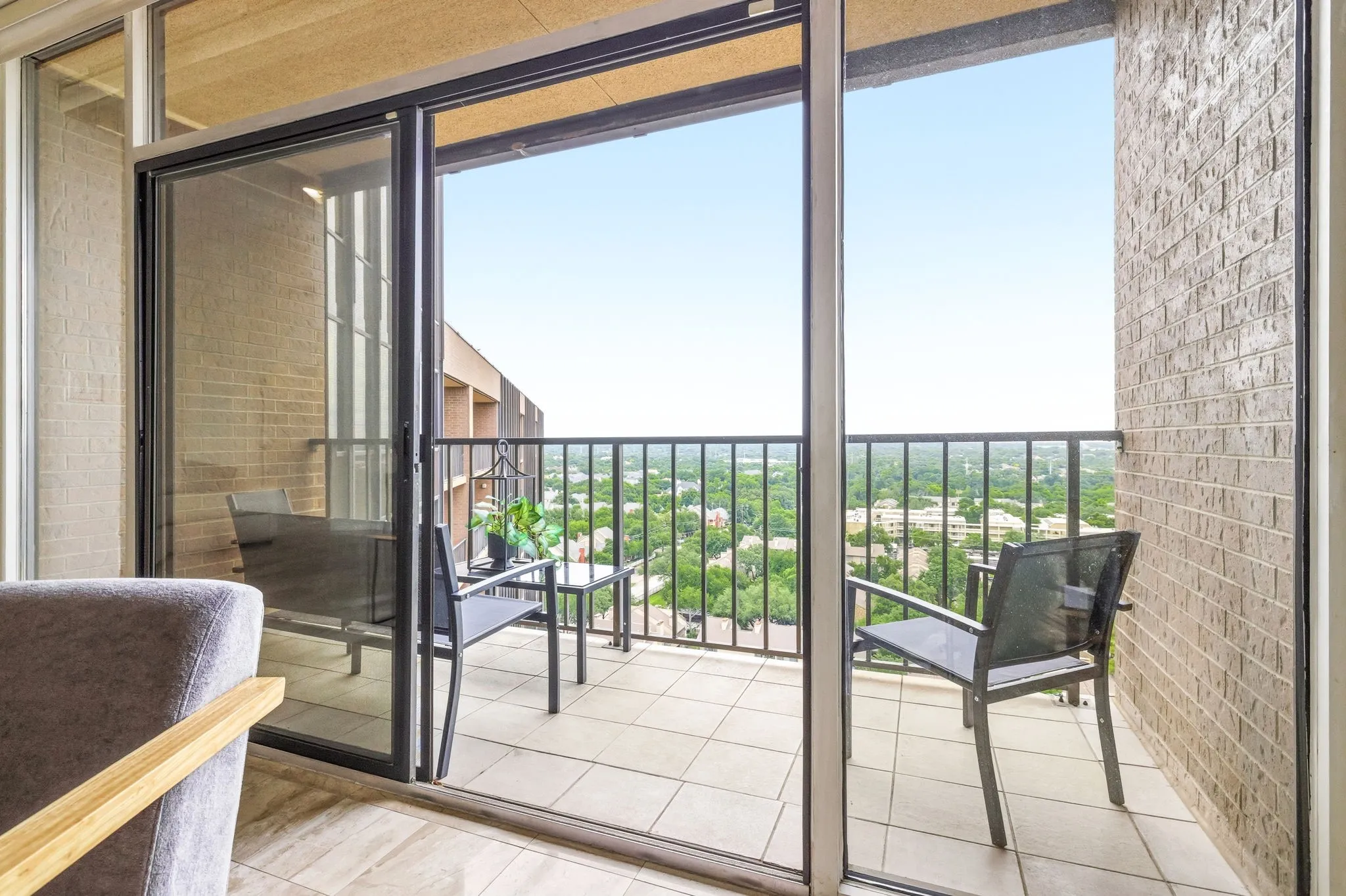 Private balcony featuring sliding glass doors, a tile floor, brick exterior wall, and metal railing