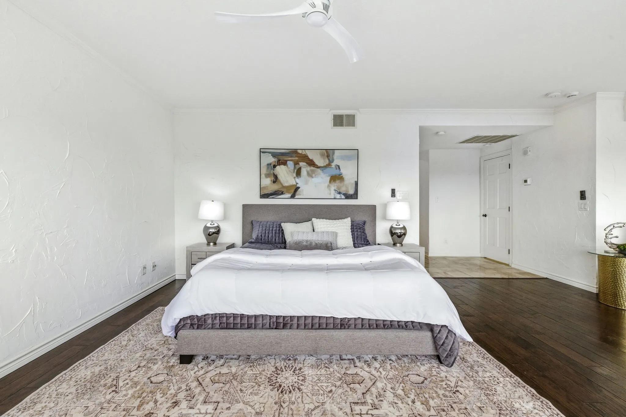 Spacious room with dark wood-finish flooring, white textured walls, and a contemporary ceiling fan