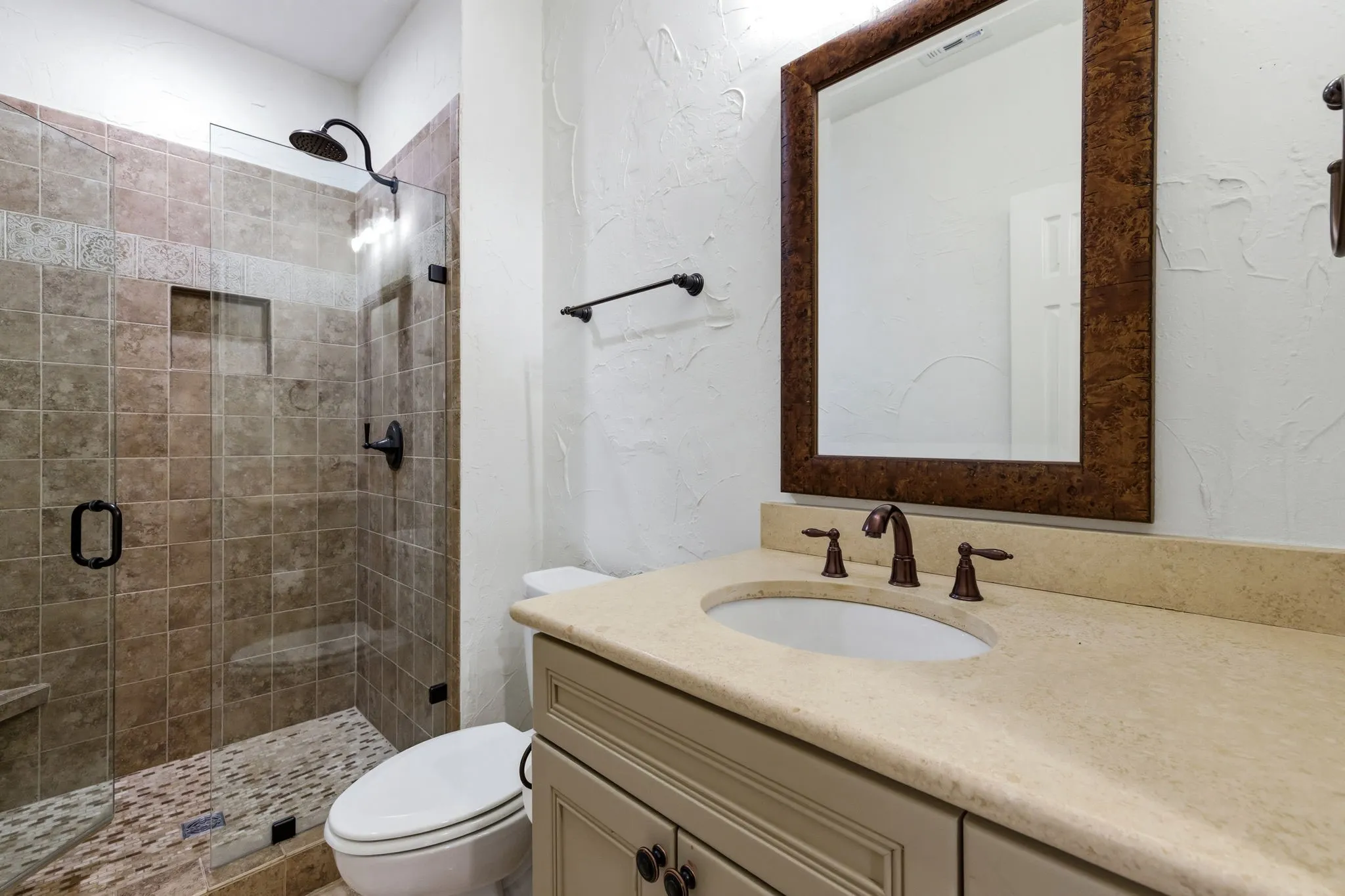 Bathroom featuring a glass-enclosed shower with tiled walls and floor, single vanity with a light-toned countertop, and an ornate framed mirror
