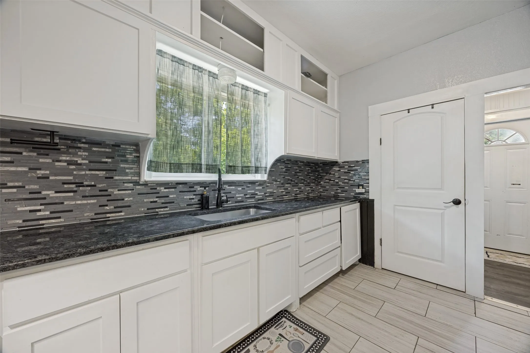 Kitchen featuring white shaker-style cabinetry, dark speckled countertops, and a full-height mosaic tile backsplash