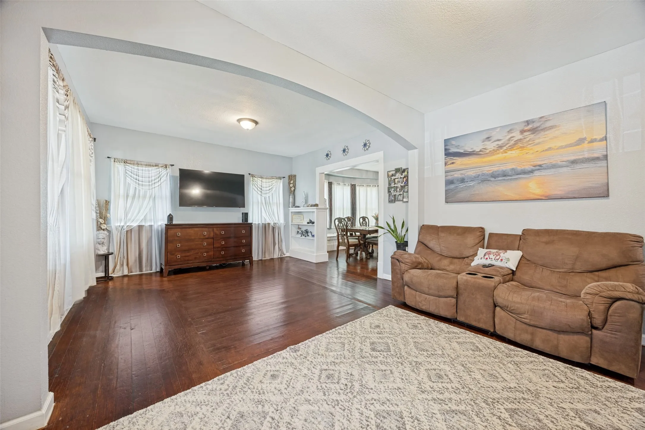 Spacious living area featuring rich wood-finish flooring and an arched doorway