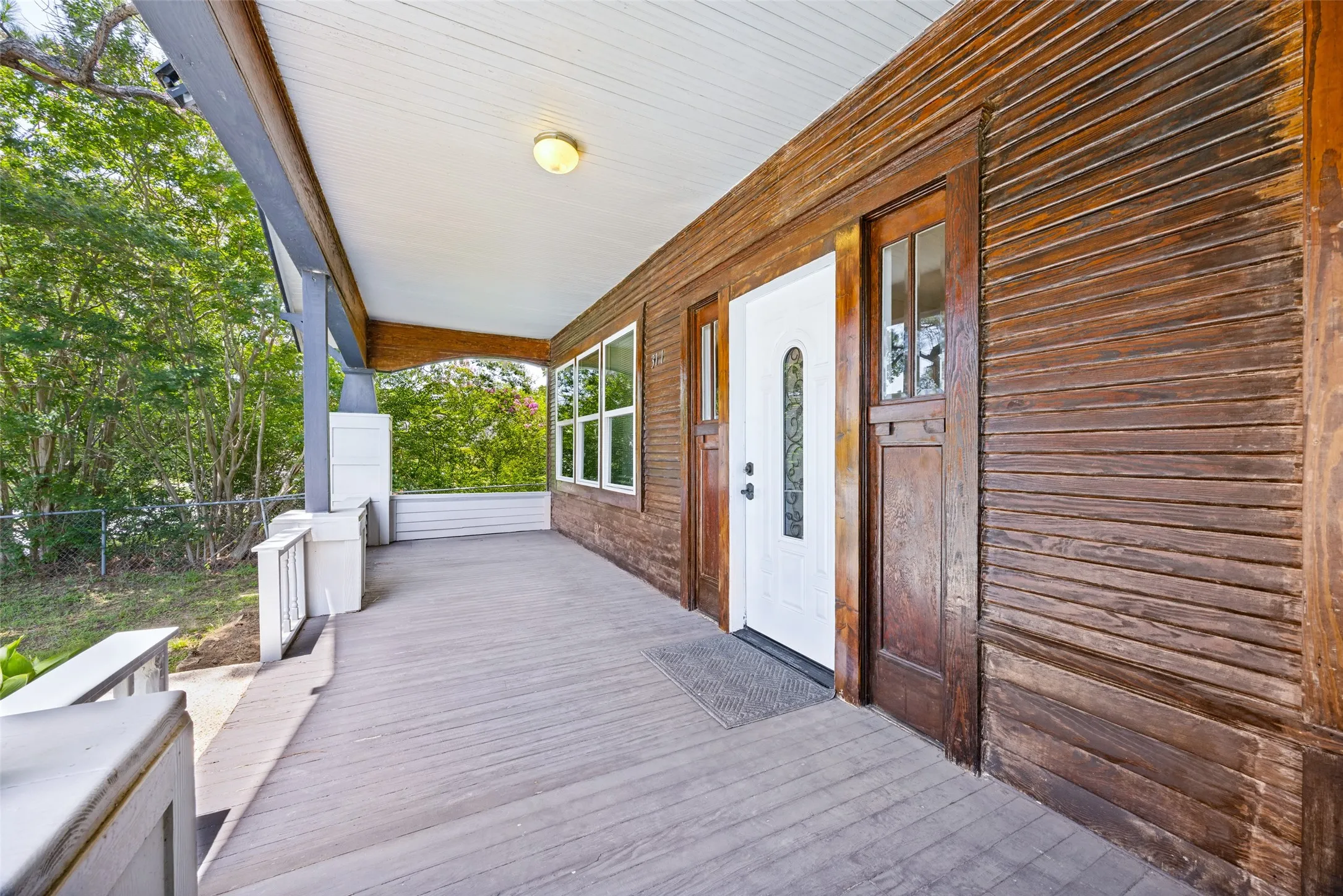 Expansive covered front porch featuring wood-finish flooring, white railing, and a beadboard ceiling with an overhead light fixture