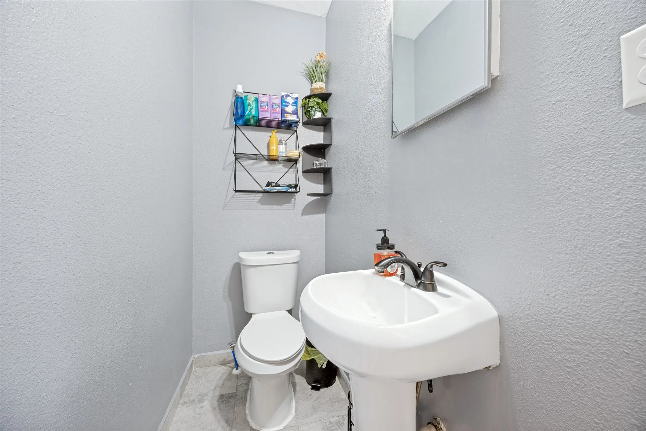 Compact bathroom featuring a white pedestal sink with a dark-finish faucet, a white toilet, and light-grey textured walls