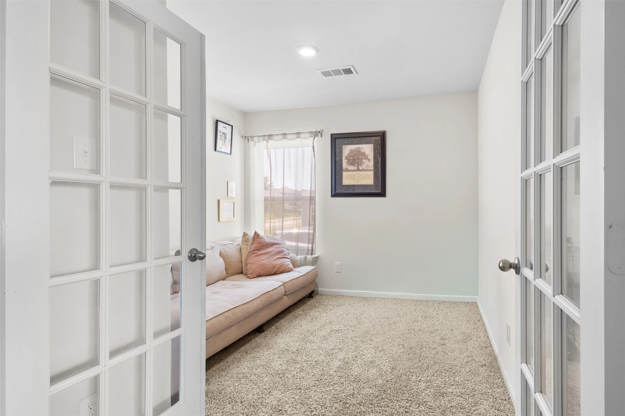 Room featuring double French doors with white frames and clear glass panes, light beige carpet, and white walls