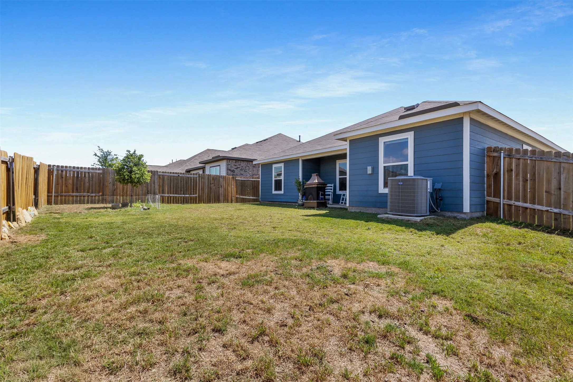 Expansive backyard featuring a privacy fence, mature tree, and a blue siding exterior with white trim