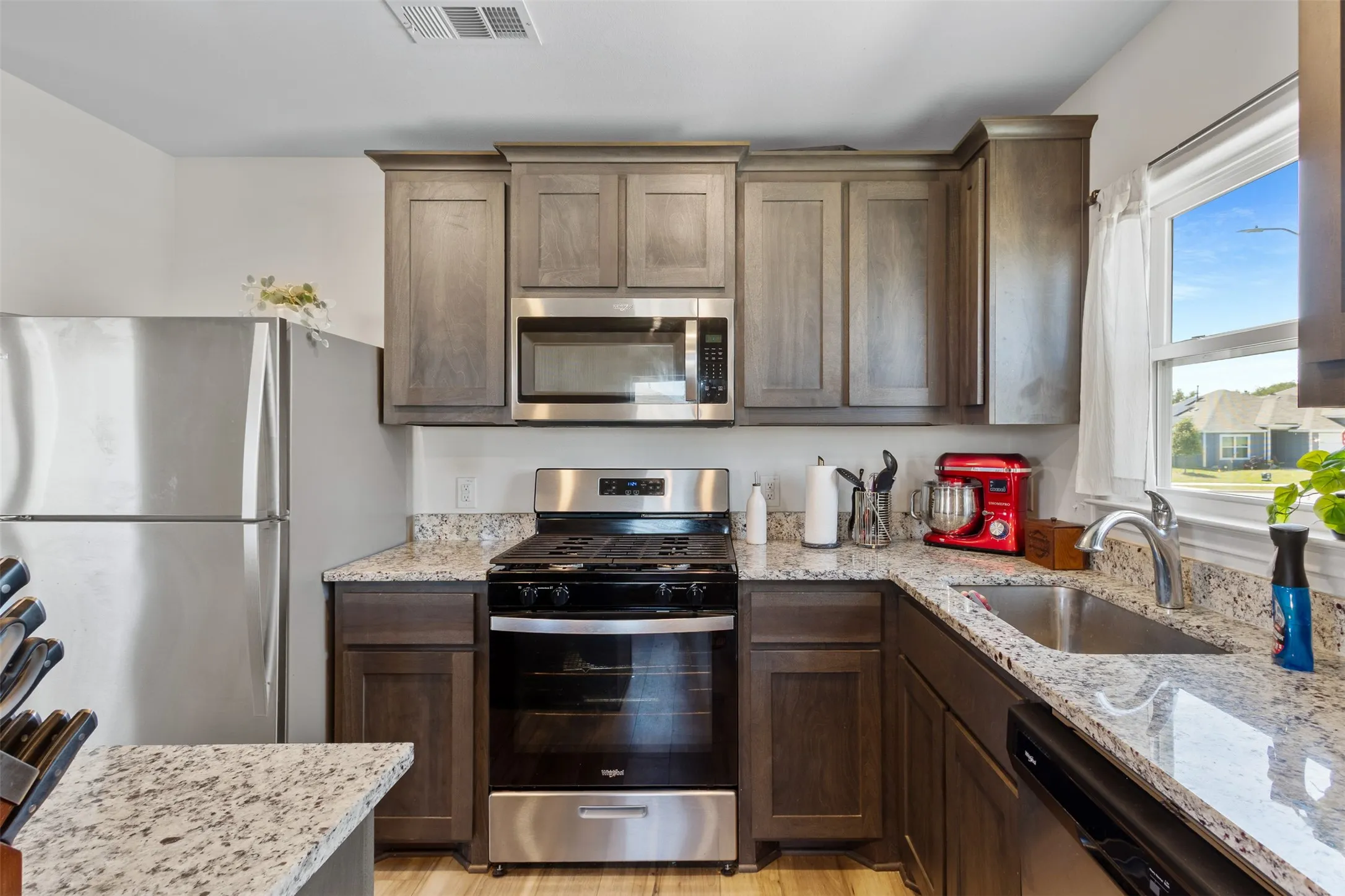 Kitchen featuring stainless steel appliances, speckled stone countertops, and wood-finish cabinetry