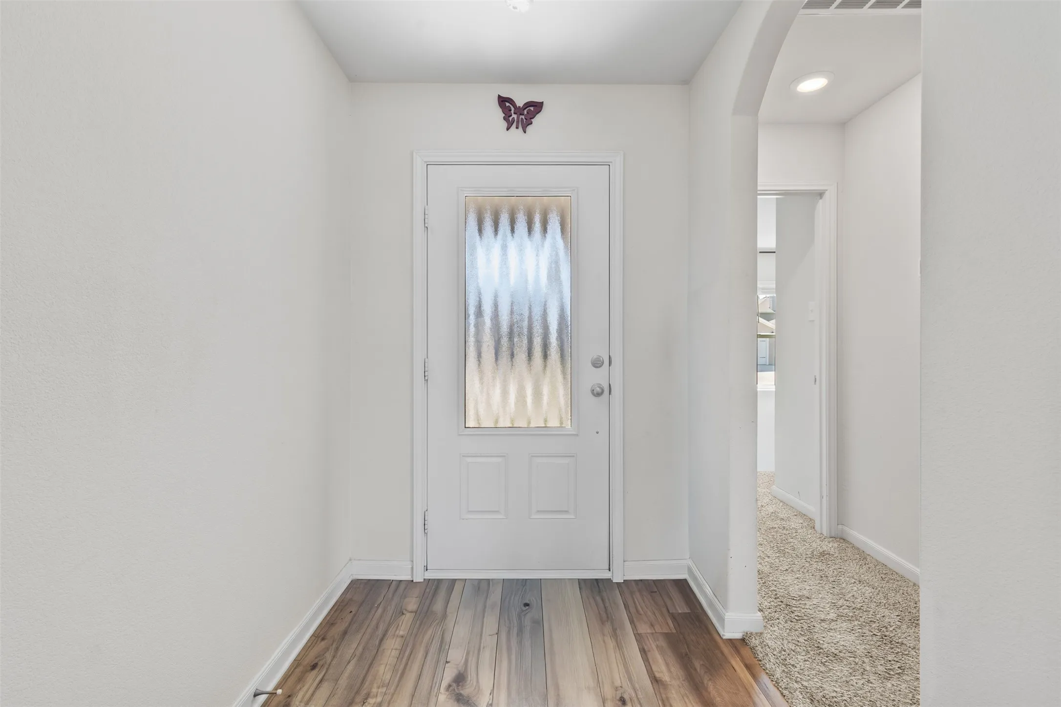 Entryway featuring a white door with a privacy glass insert, wood-finish flooring, and white baseboards