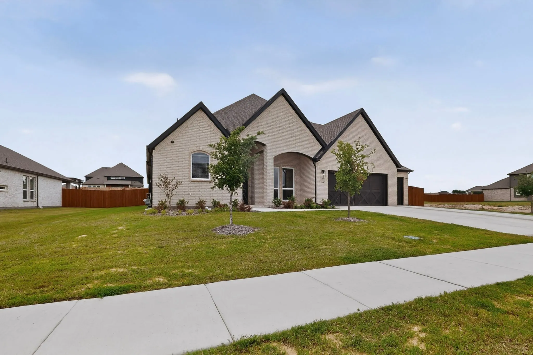 Contemporary brick residence featuring a prominent gabled roofline, an integrated two-car garage, established front landscaping, and a concrete driveway