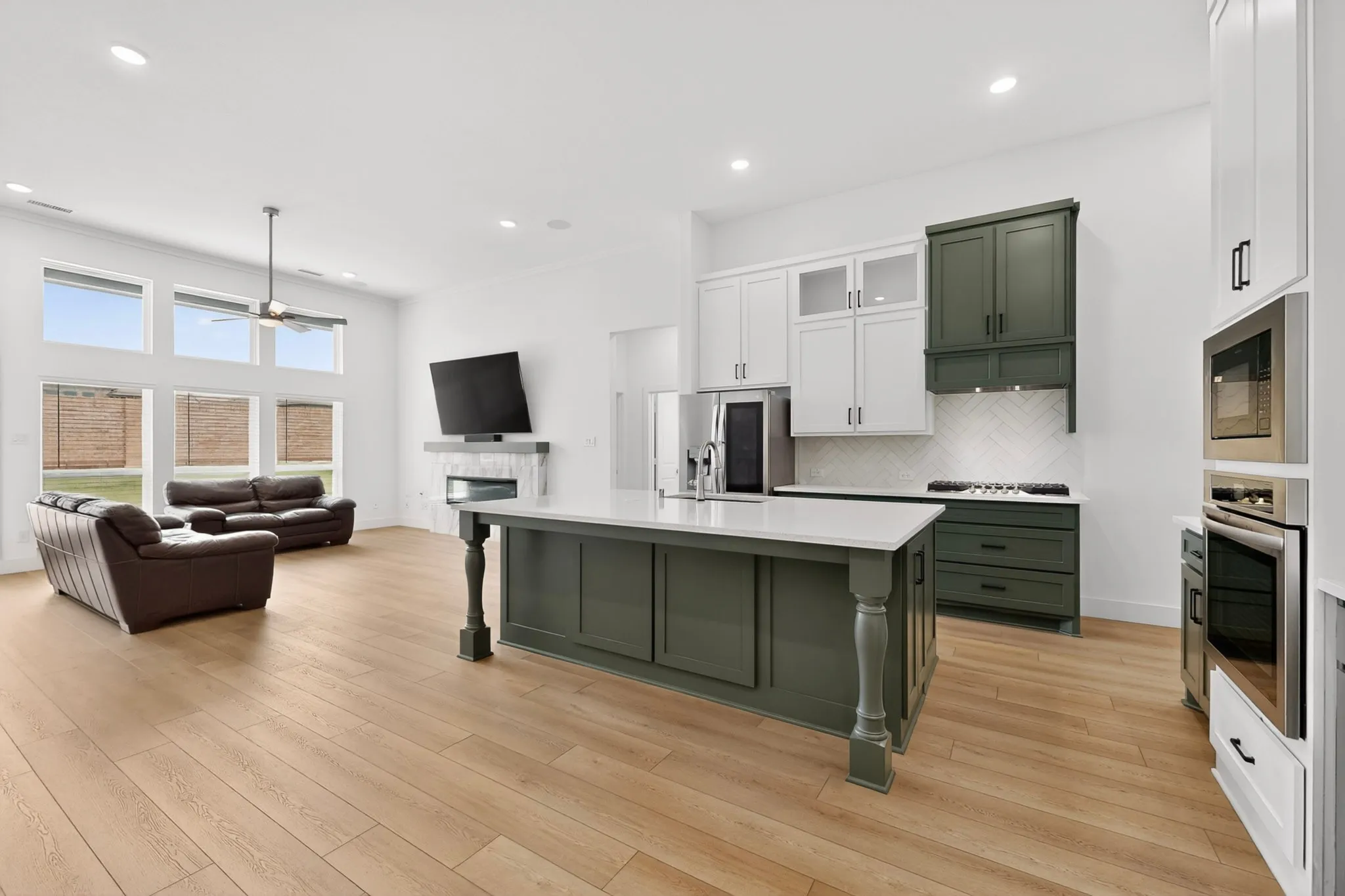 Open-concept living space featuring a central kitchen island with seating, a gas range with a herringbone tile backsplash, integrated stainless steel appliances, wood-finish flooring, and a living area with a fireplace