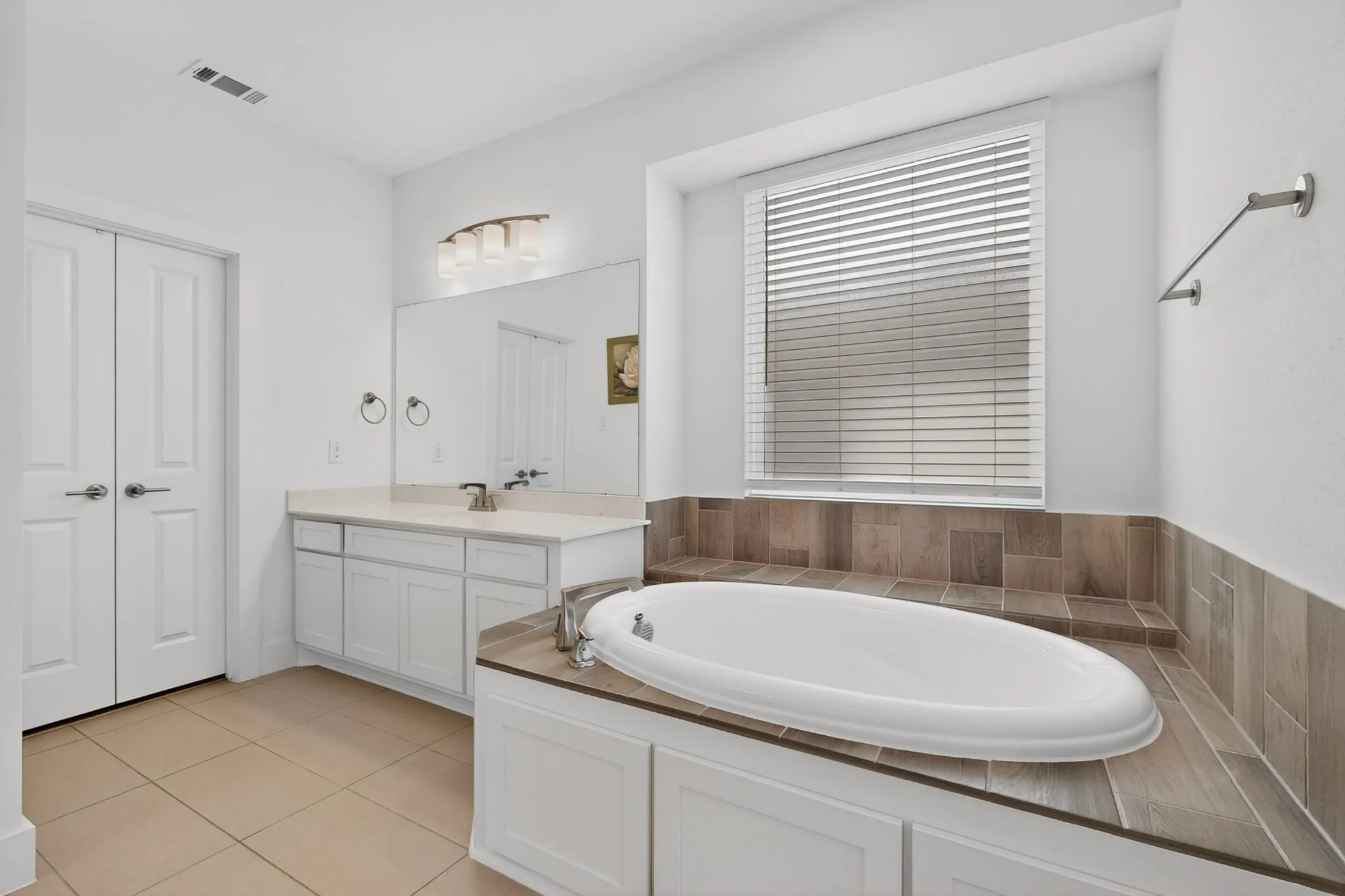 Soaking tub with surrounding wood-finish tile and window with blinds