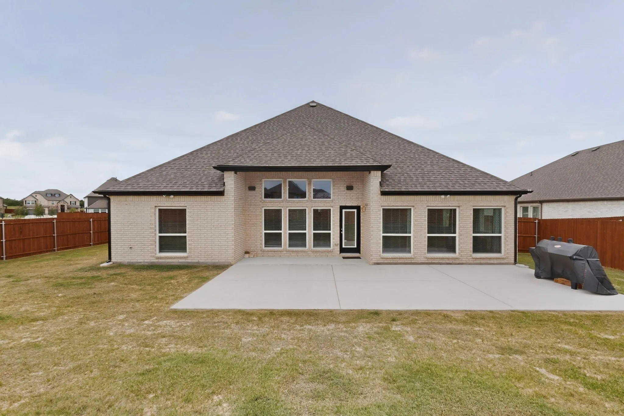 Rear exterior featuring light-colored brick, a dark shingle roof, and a concrete patio