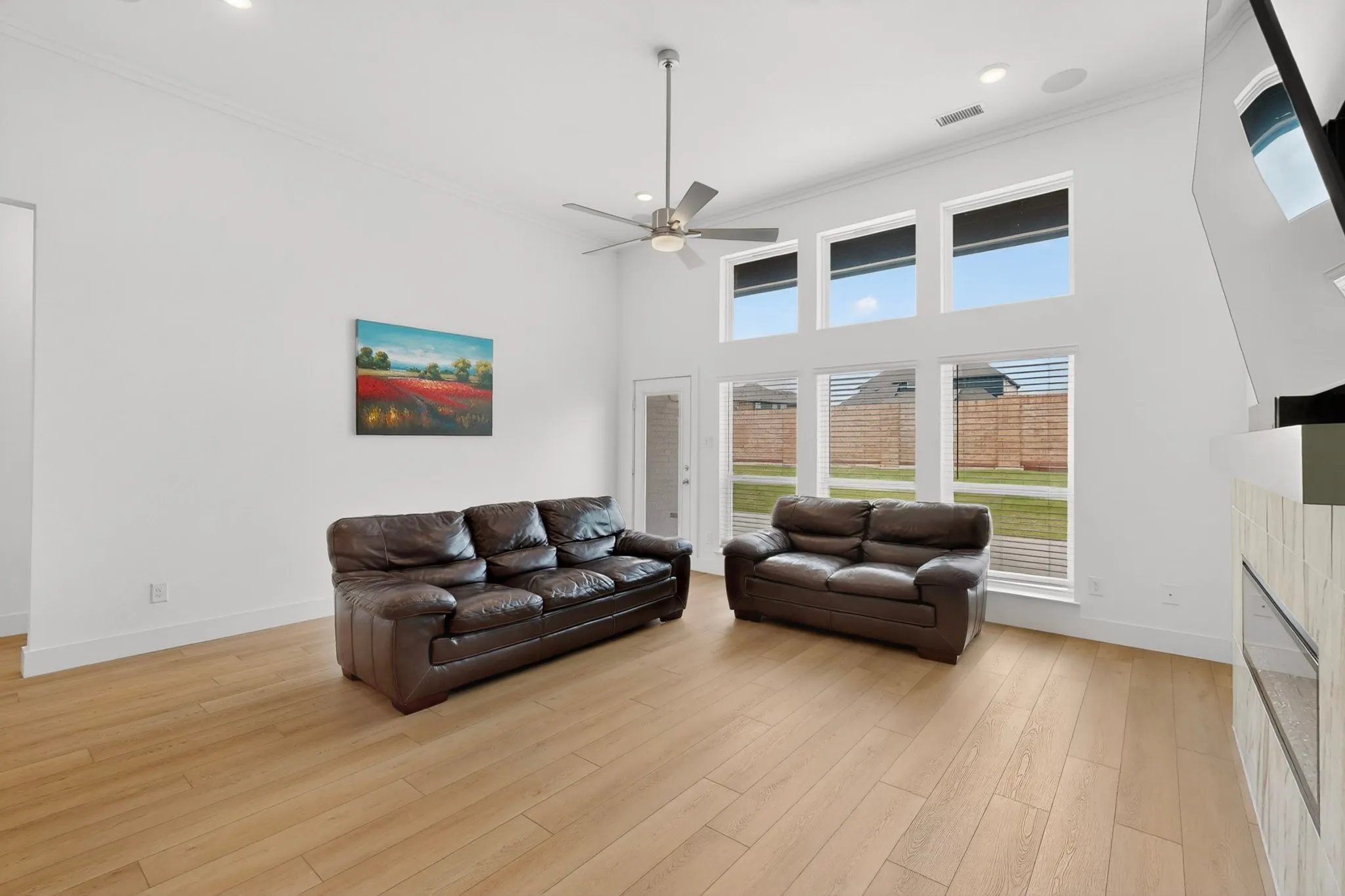 Living area featuring high ceilings, wood-finish flooring, a contemporary ceiling fan, and multiple large windows for abundant natural light