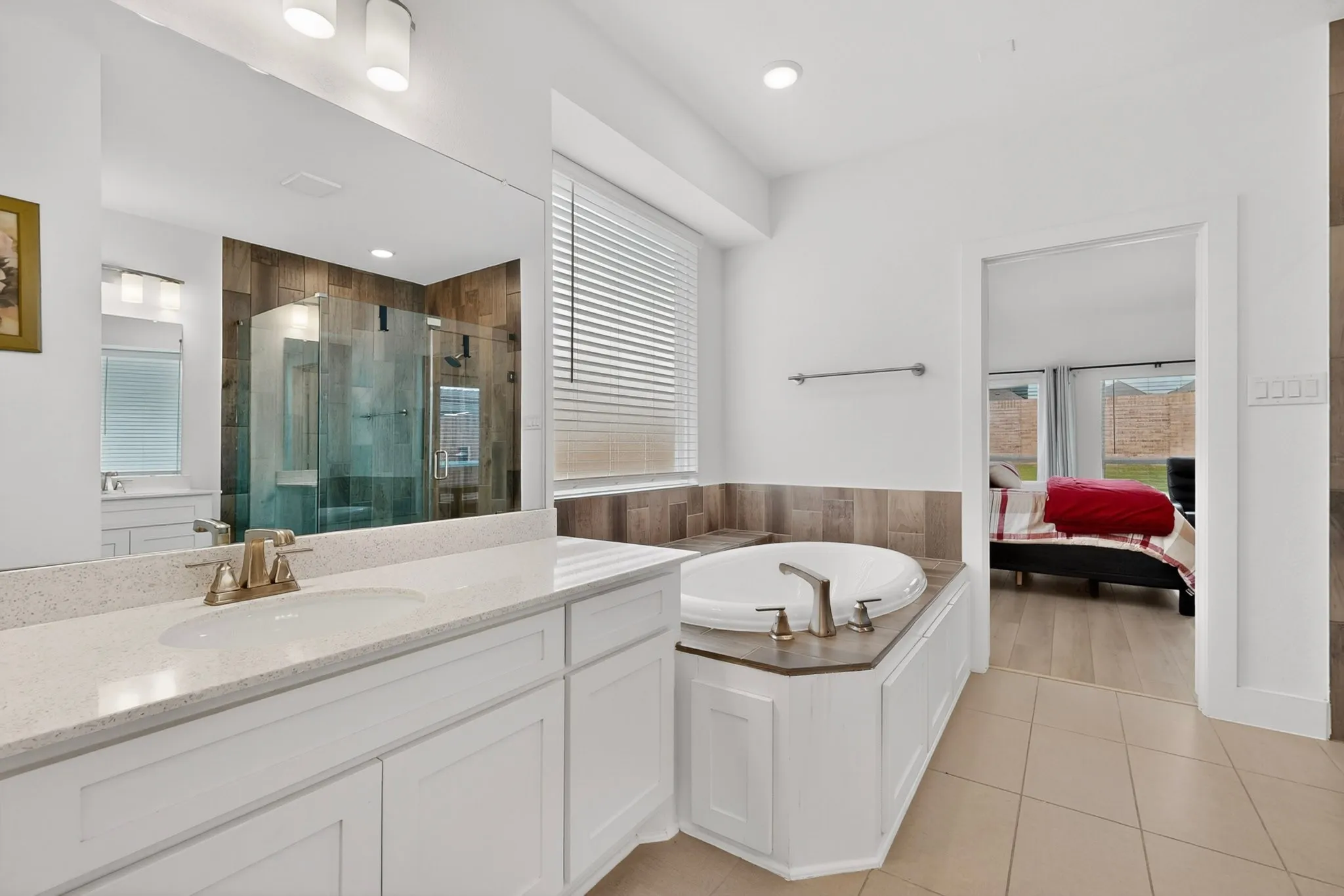Bathroom featuring a built-in soaking tub, a separate glass-enclosed shower, a double vanity with stone-look countertops, and tile flooring
