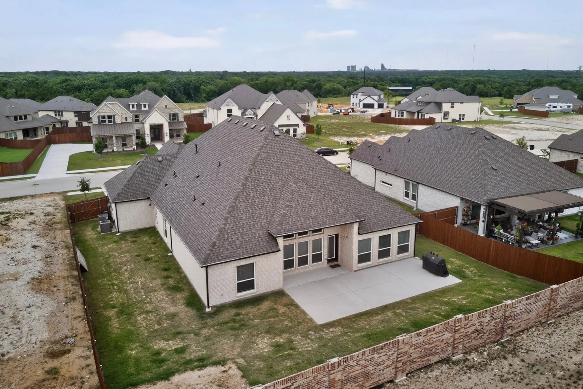 Rear exterior featuring a spacious concrete patio, multiple large windows, and a mature treeline in the distance
