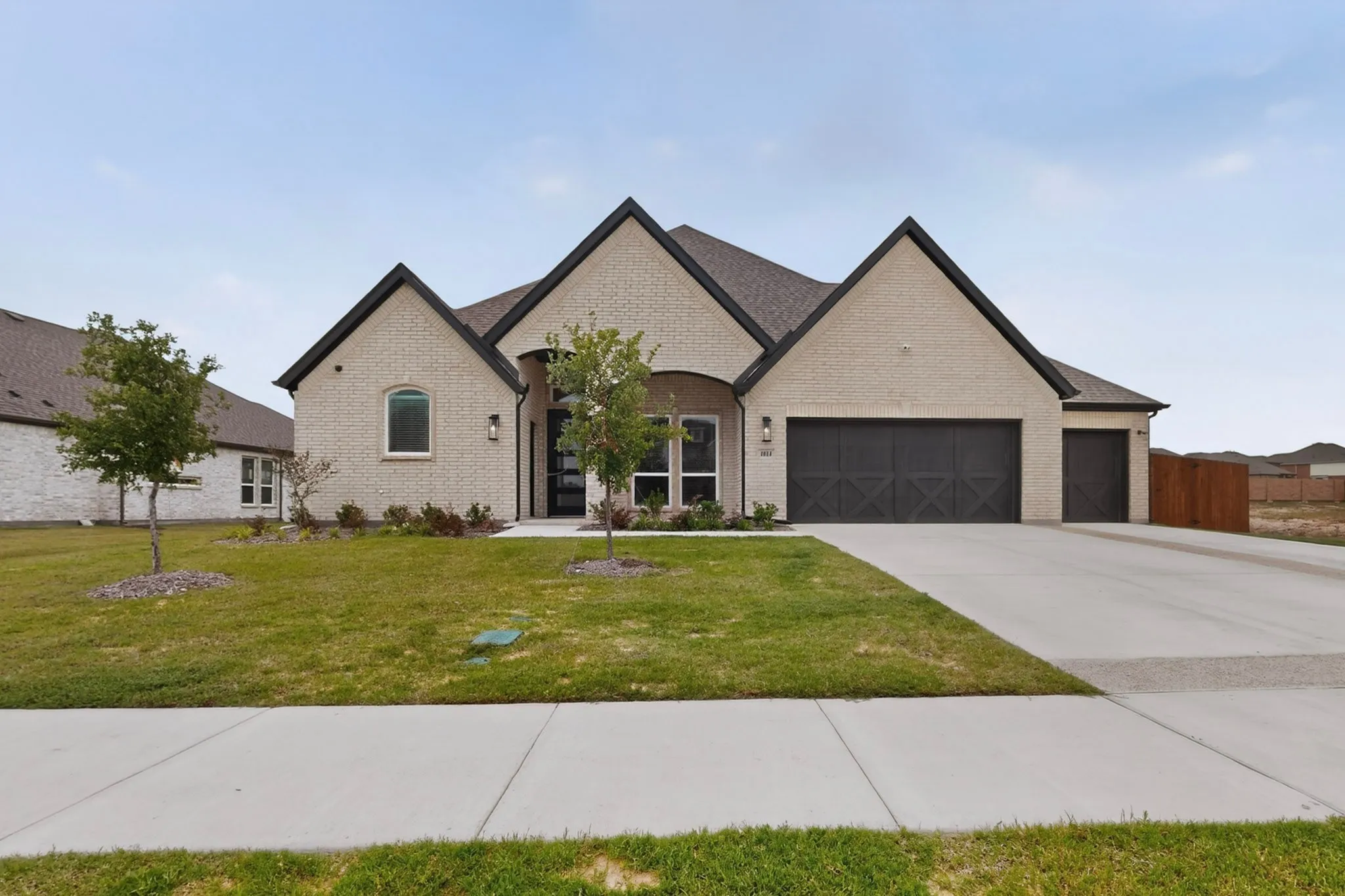 Contemporary brick exterior featuring a multi-gabled roofline, a three-car garage with decorative doors, and a concrete driveway